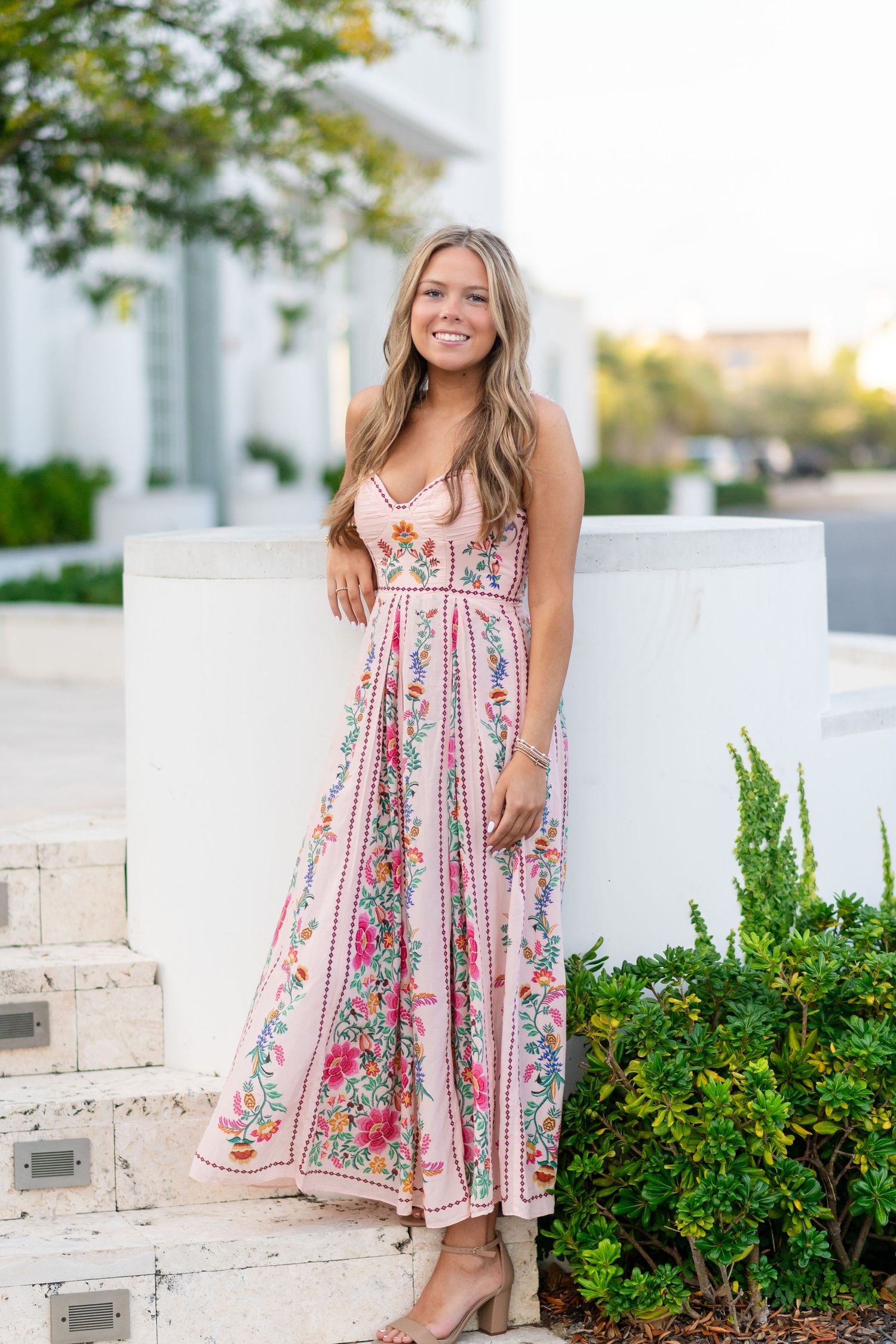 A floral sundress is showcased against white walls and lush greenery in an outdoor setting.