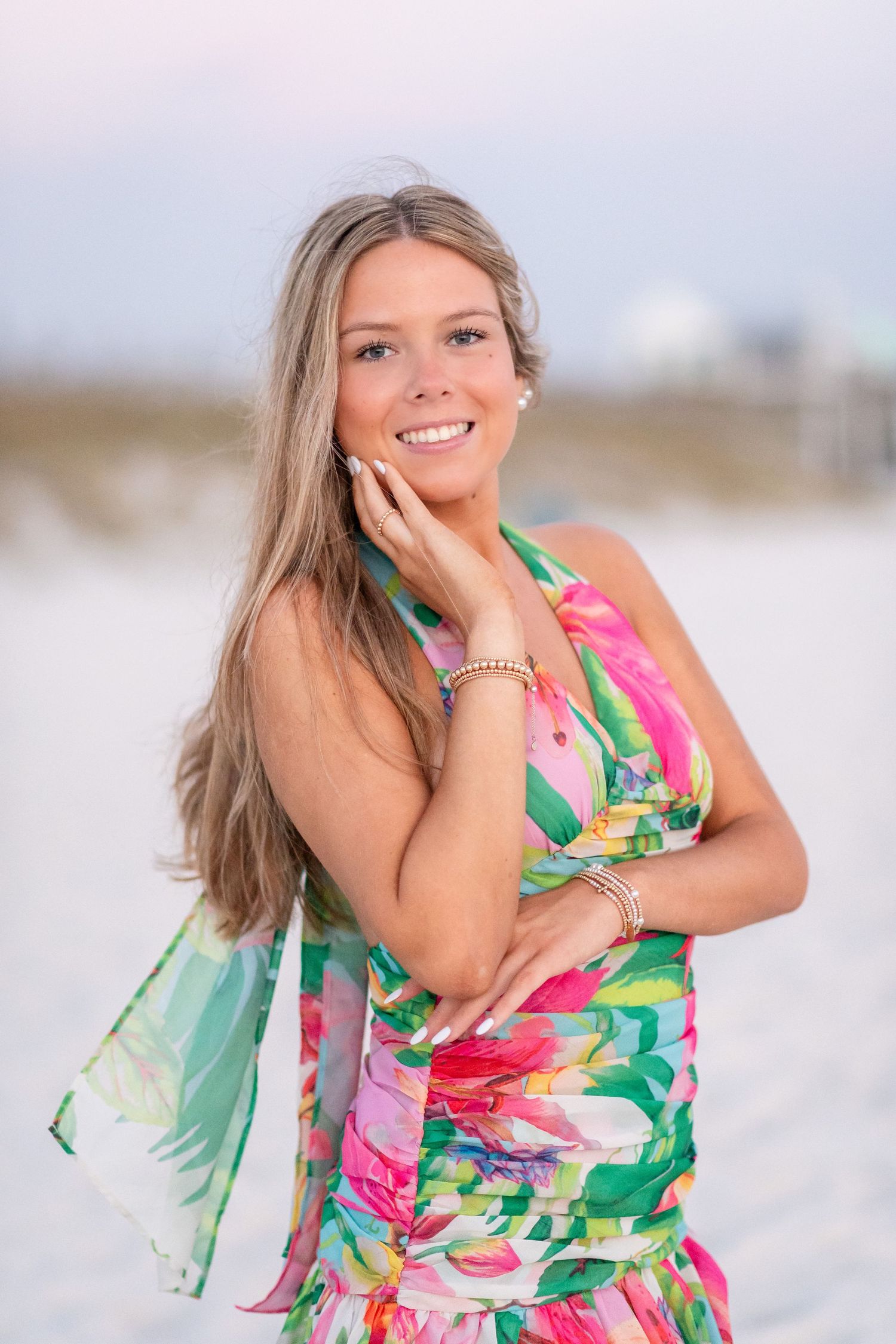 A person in a vibrant floral halter dress poses on a white sandy beach in a series of casual portraits.