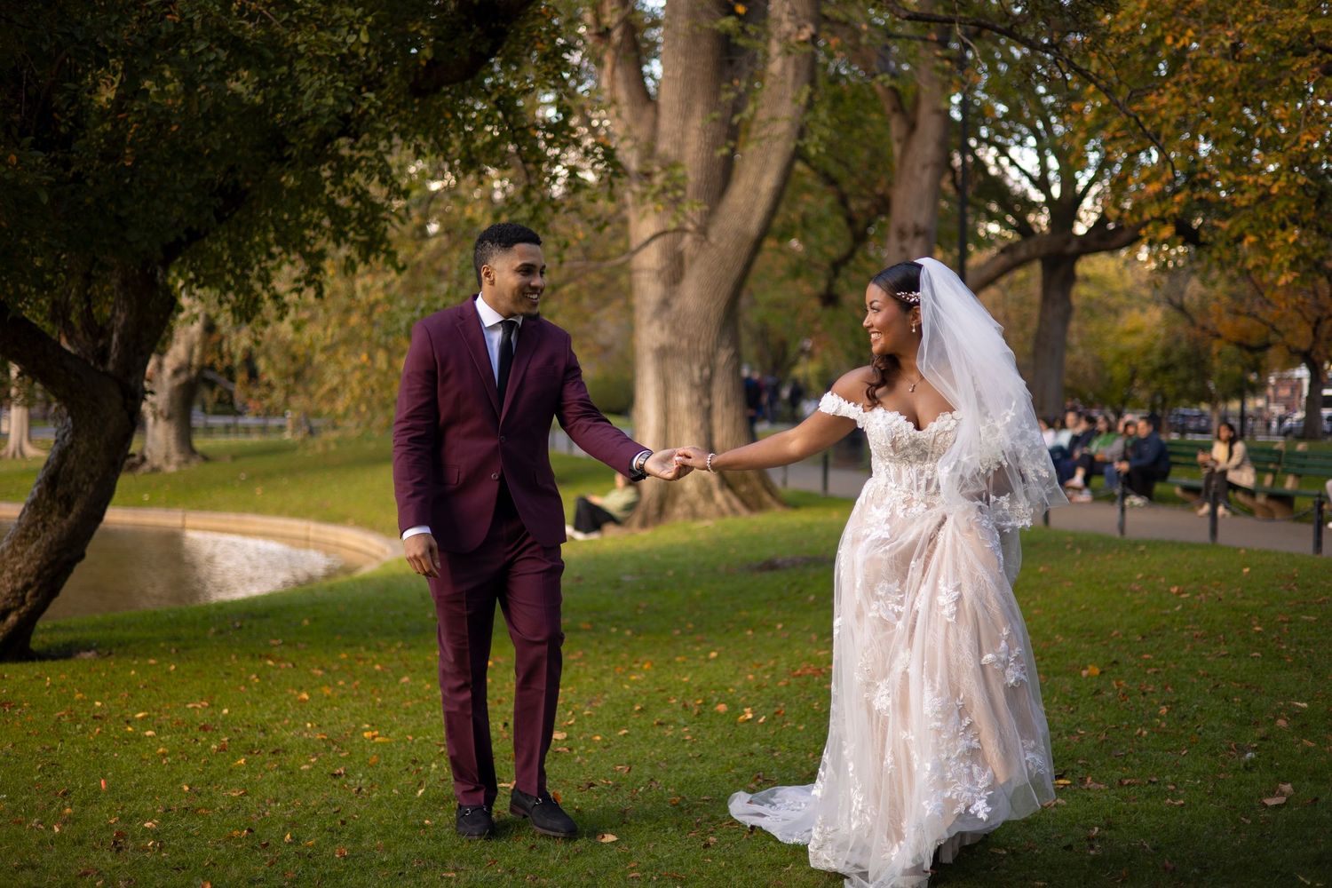 Couple in formal wedding attire walking and dancing together on a tree-lined path during autumn.