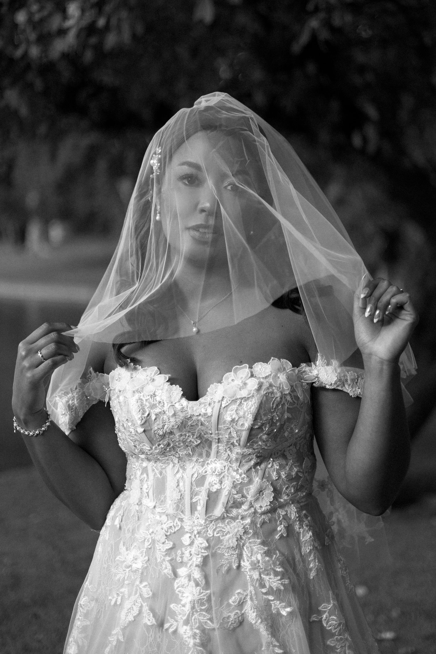 A series of black and white bridal portraits showing a white lace wedding dress and flowing veil in an outdoor setting.