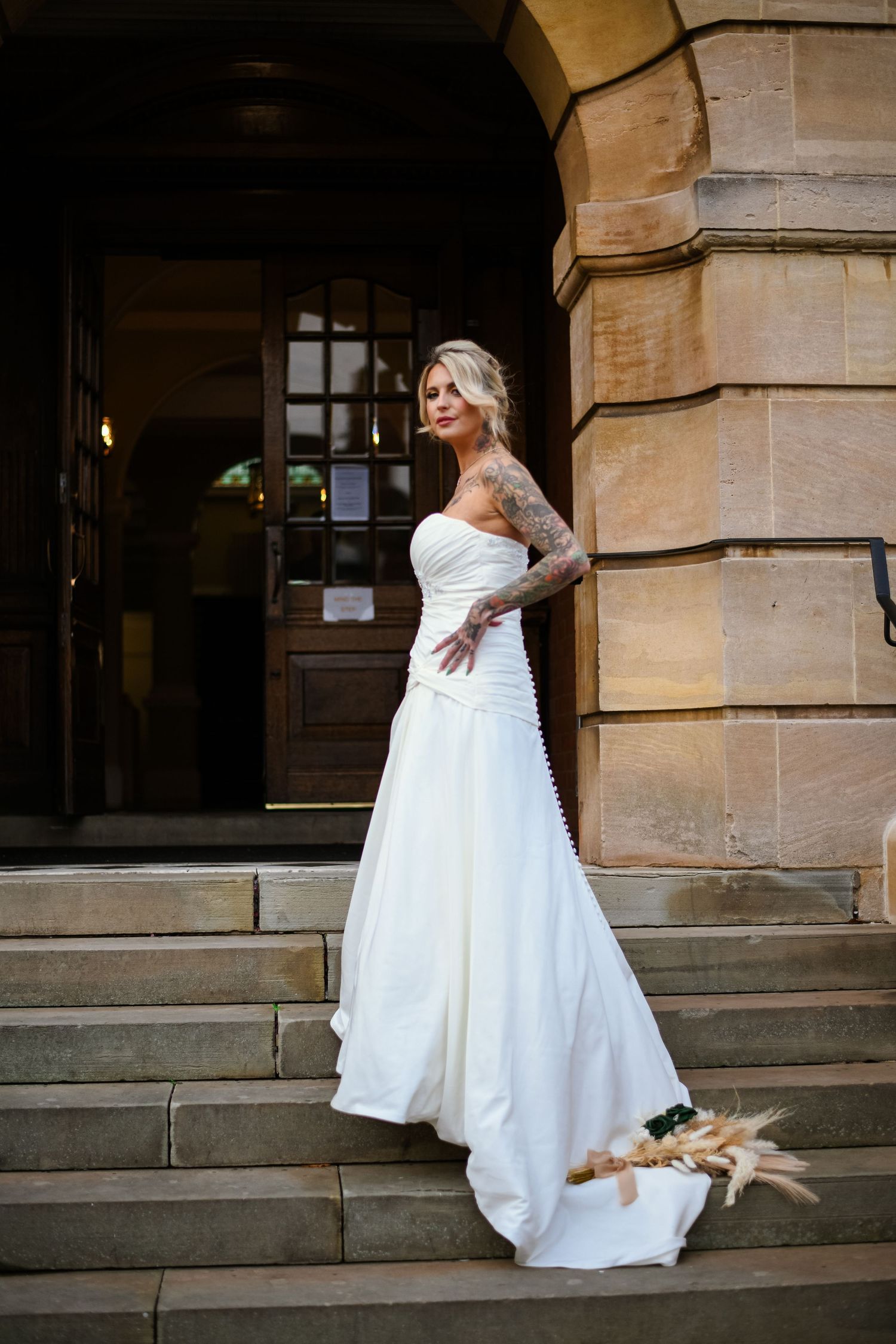 A bride in a white beaded wedding dress holding a red and white rose bouquet smiles during her wedding celebration.
