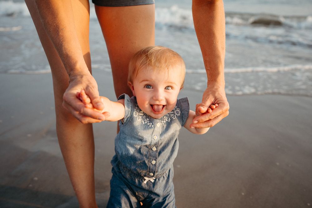 A child plays joyfully in the shallow ocean waves at the beach during lifestyle family photography session. Wilmington, NC Family Photos