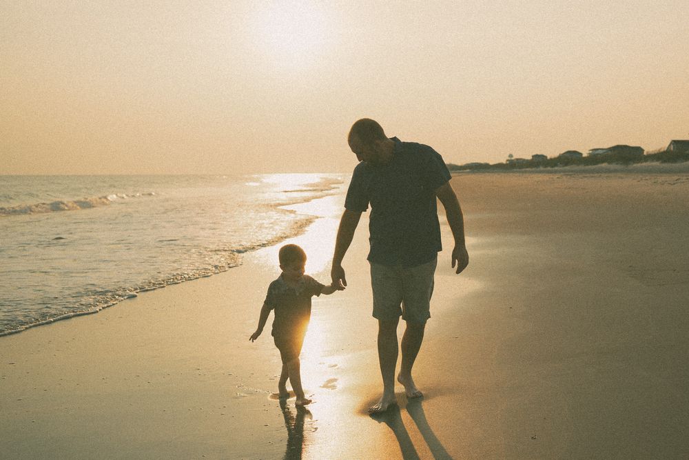 Warm-toned silhouettes of beachgoers walking along the shoreline during golden hour. Lifestyle Family Photographer Wilmington NC