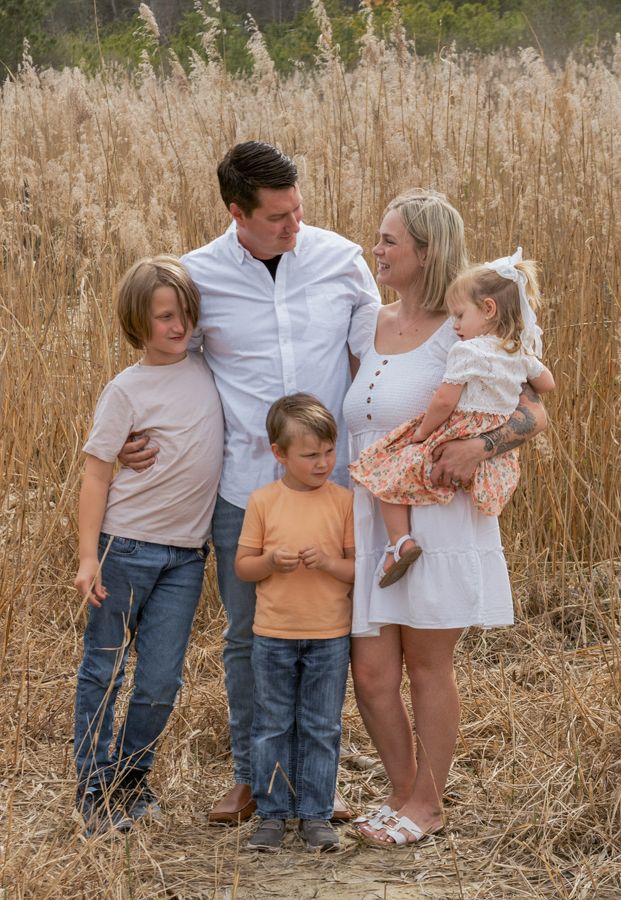 family session on the beach. Grandpa, grandma, mom, dad, and baby all wearing white with beachy grasses in the background