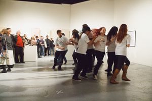 Wide shot of people gathered in a large white gallery space for a performance.
