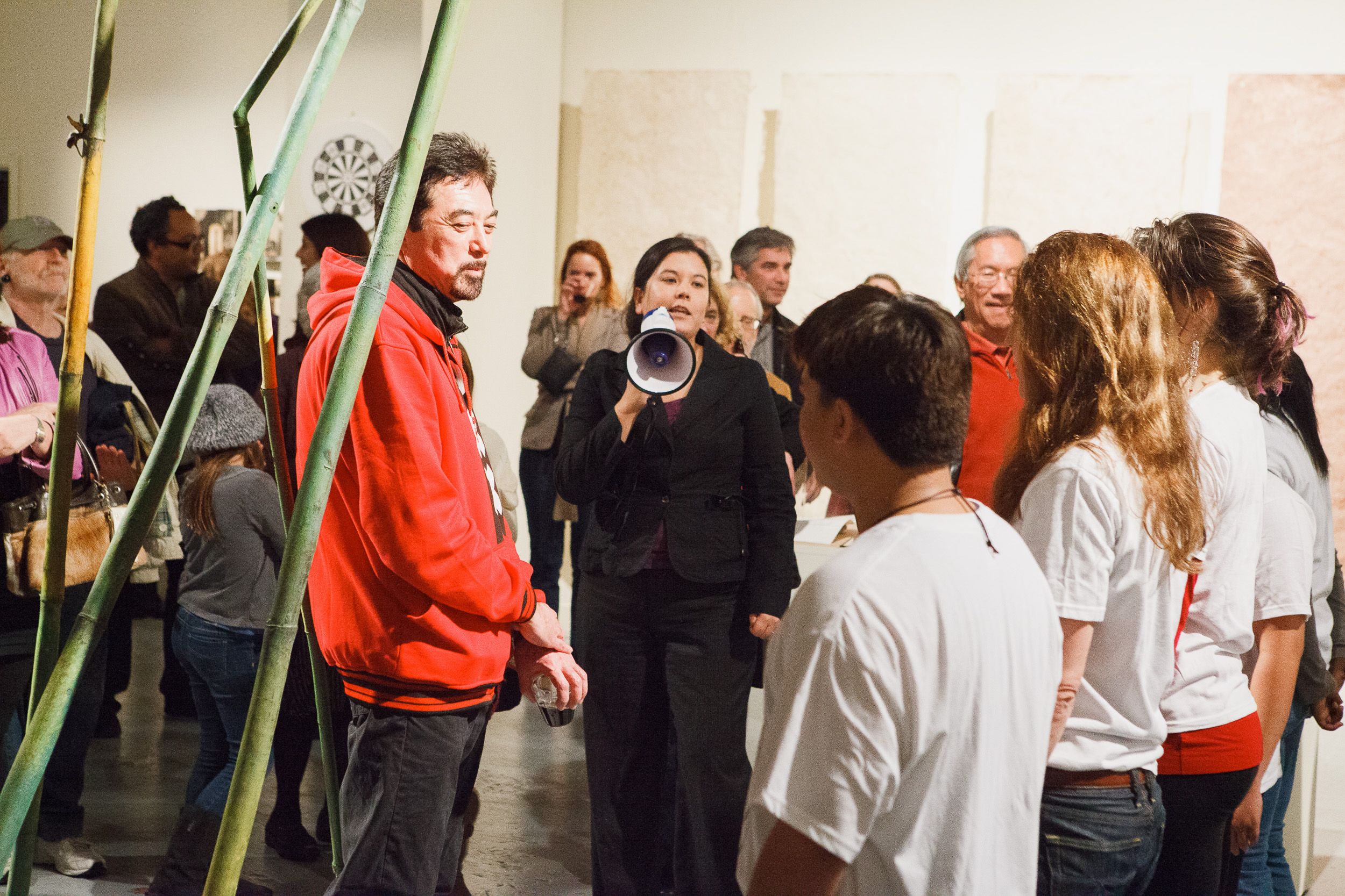 People in white shirts gathered in an art gallery with green props or banners.