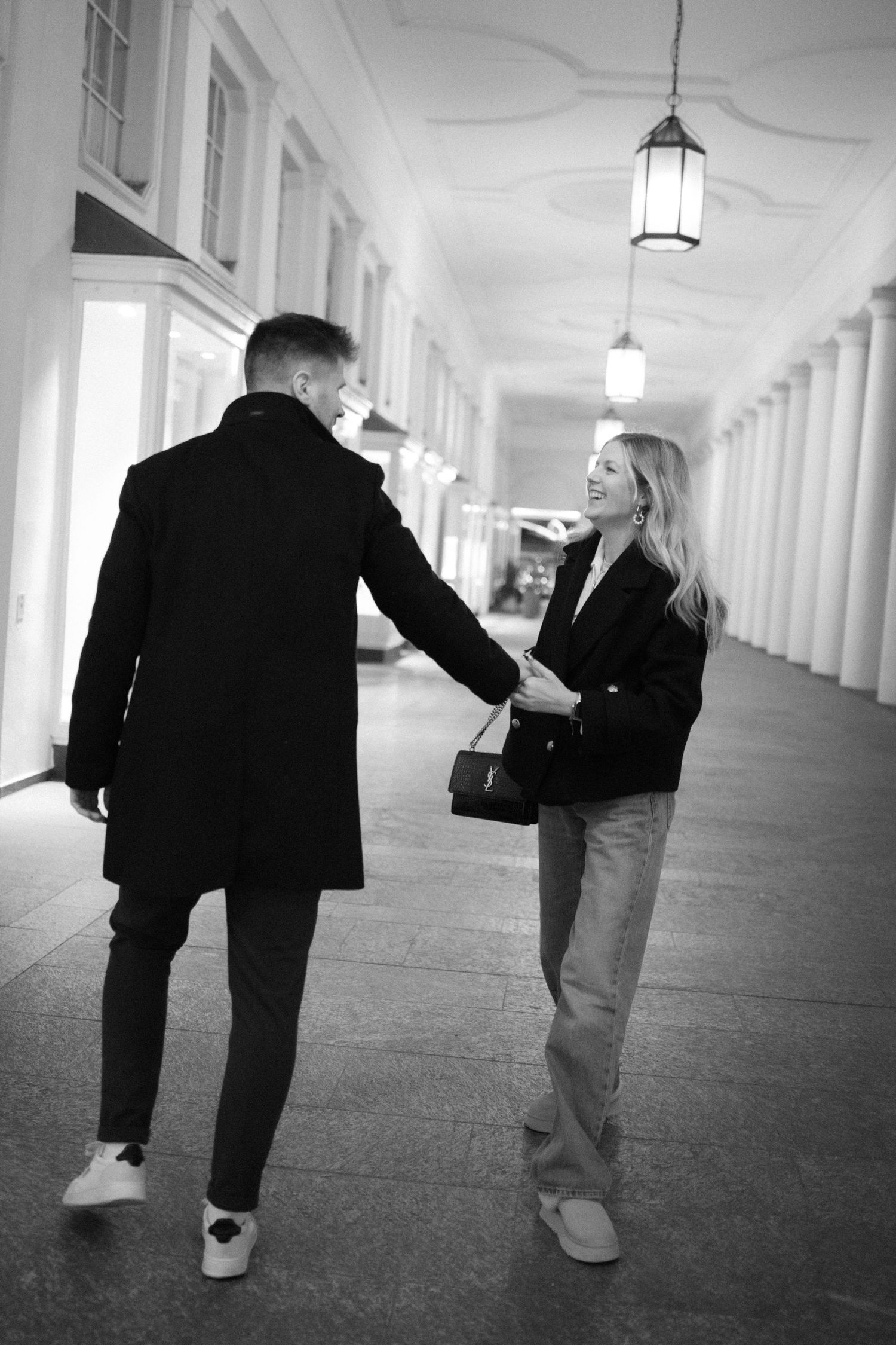 Black and white sequence showing two people walking down an elegant corridor with pendant lights.