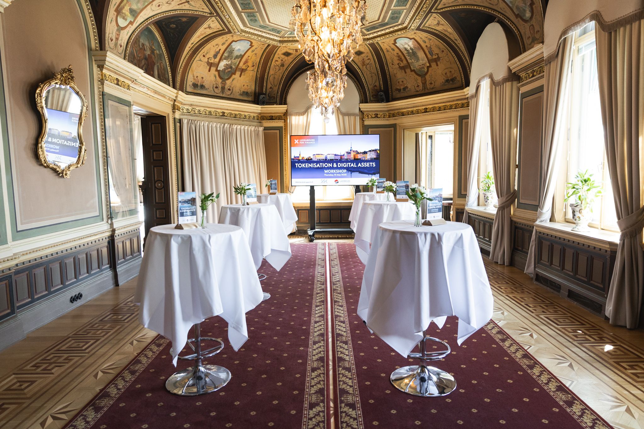 Elegant ballroom interior with ornate gold details, crystal chandeliers, and red carpeting in a luxurious palace setting.