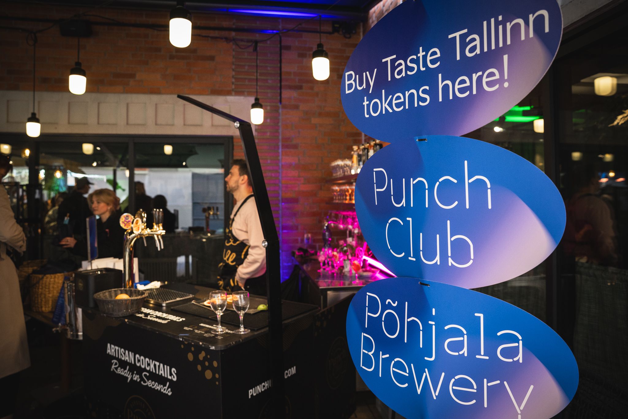 A series of illuminated blue signs and displays at night showcasing various establishments including a brewery and club.