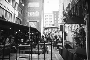 Black and white urban street scene with storefronts and pedestrians walking along a city sidewalk.