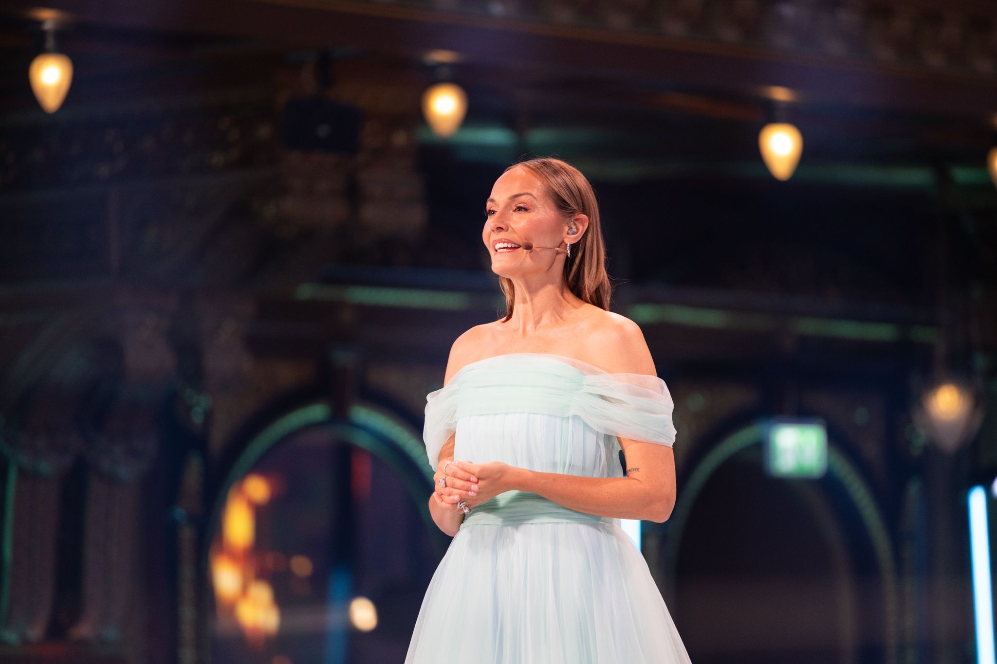 A person in a white flowing dress twirls gracefully on a dark stage with warm lighting in the background.
