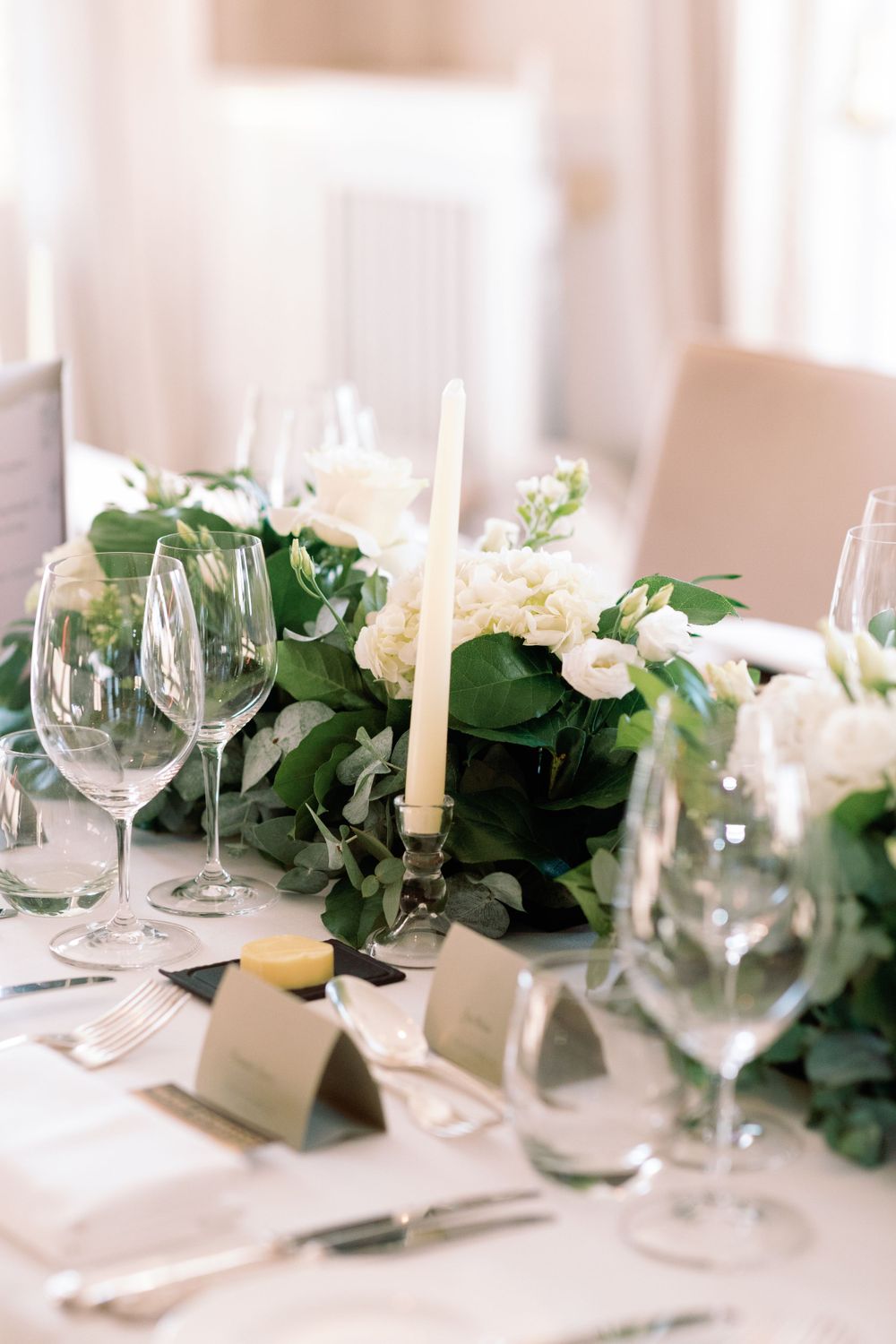 Elegant wedding table setting with white flowers, greenery garland, and taper candles.