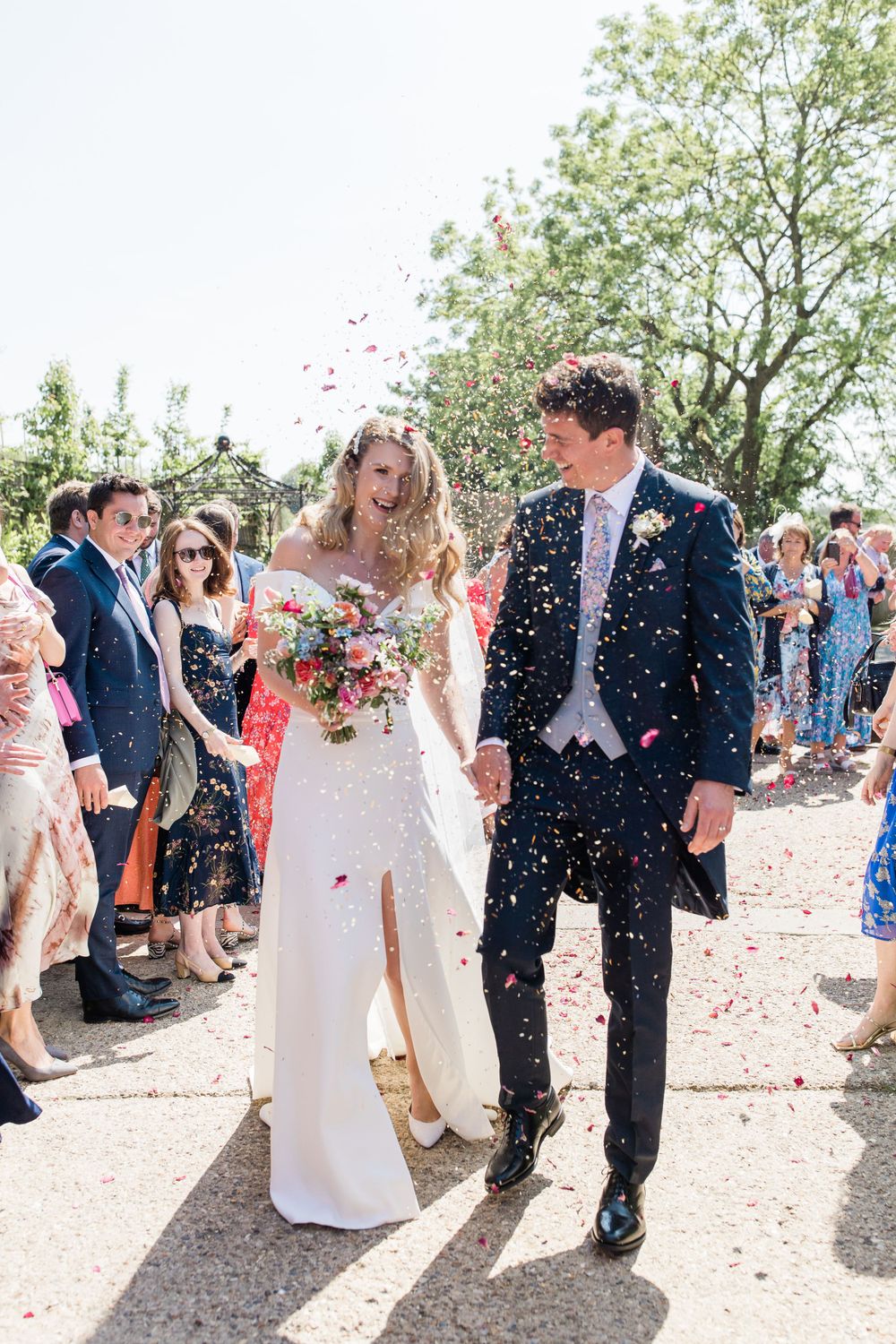 Joyful wedding exit with confetti shower along sunny garden path at The Barn at Botley Hill by Maddie Waters Photography