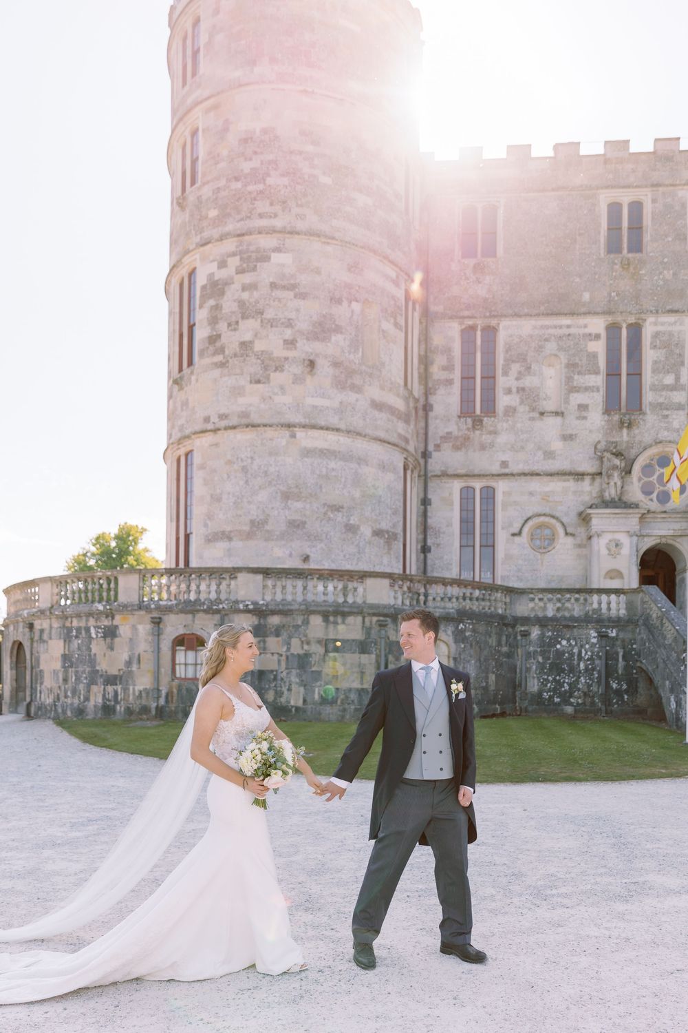 Bride and Groom walking hand in hand outside Lulworth Castle during golden hour by Maddie Waters Photography