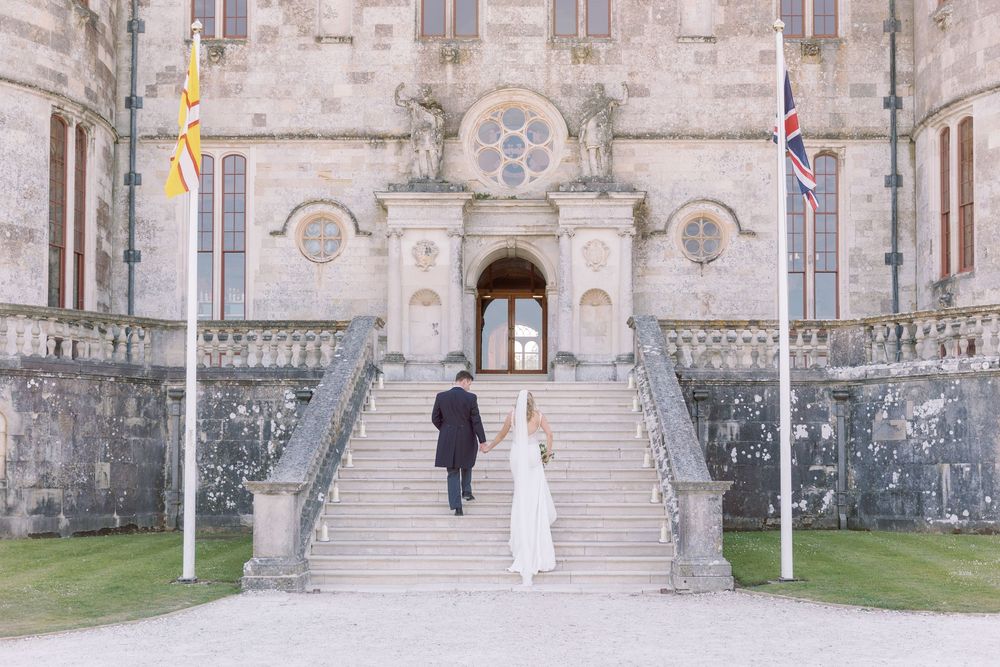 Bride and Groom walking up the grand stone steps to Lulworth Castle, by Maddie Waters Wedding Photographer.