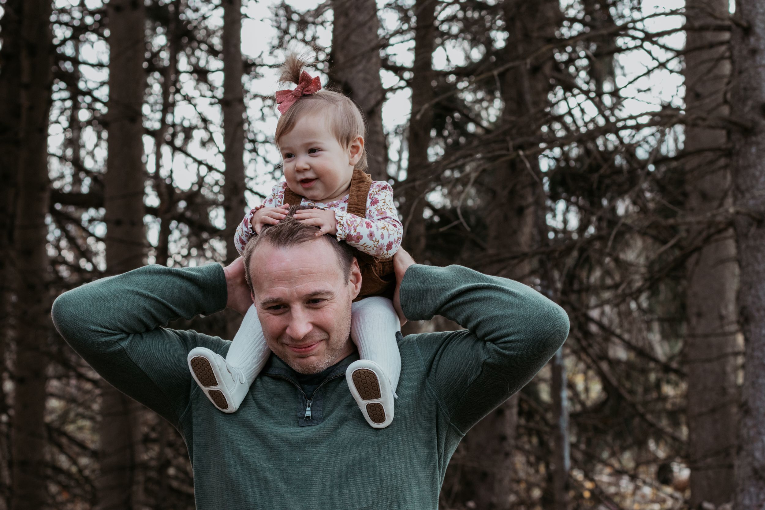 Candid family photos showing playful shoulder rides in a forest setting.
