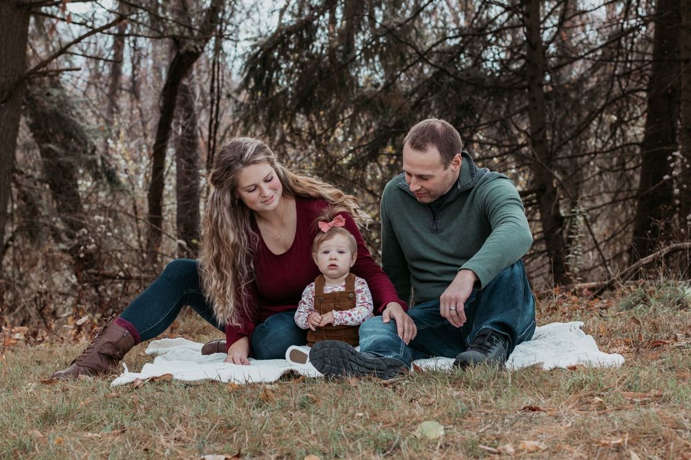 Family lying on autumn ground having candid moments together in wooded setting.