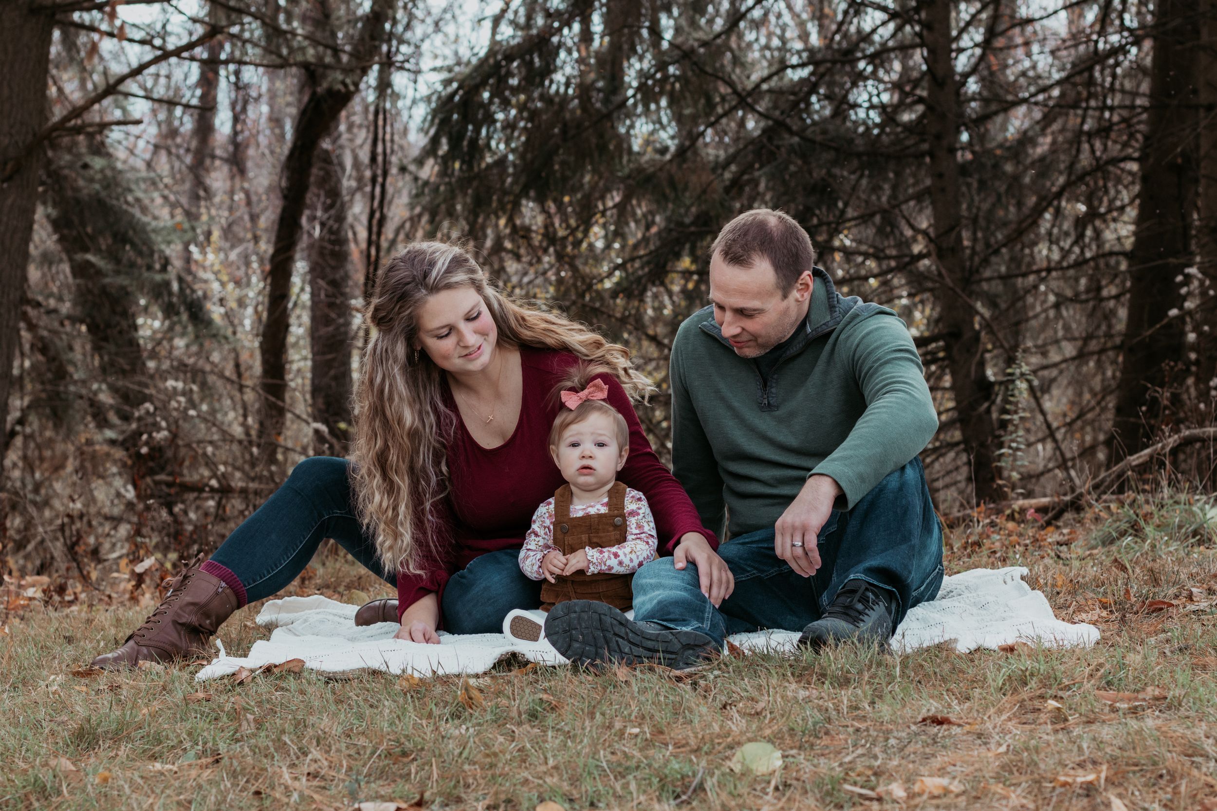 Family lying on autumn ground having candid moments together in wooded setting.