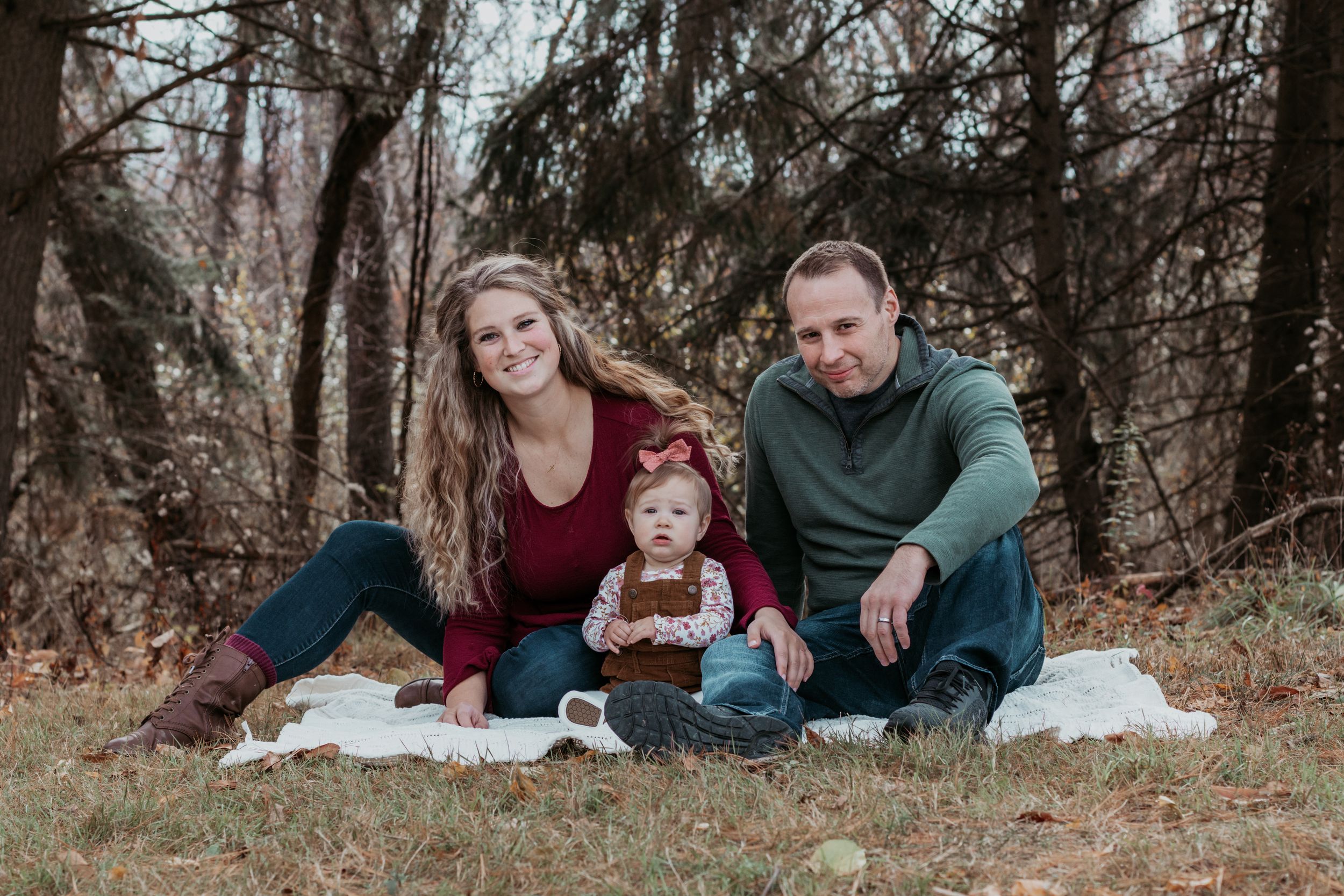 Family relaxing on fallen leaves during outdoor photo session in forest.