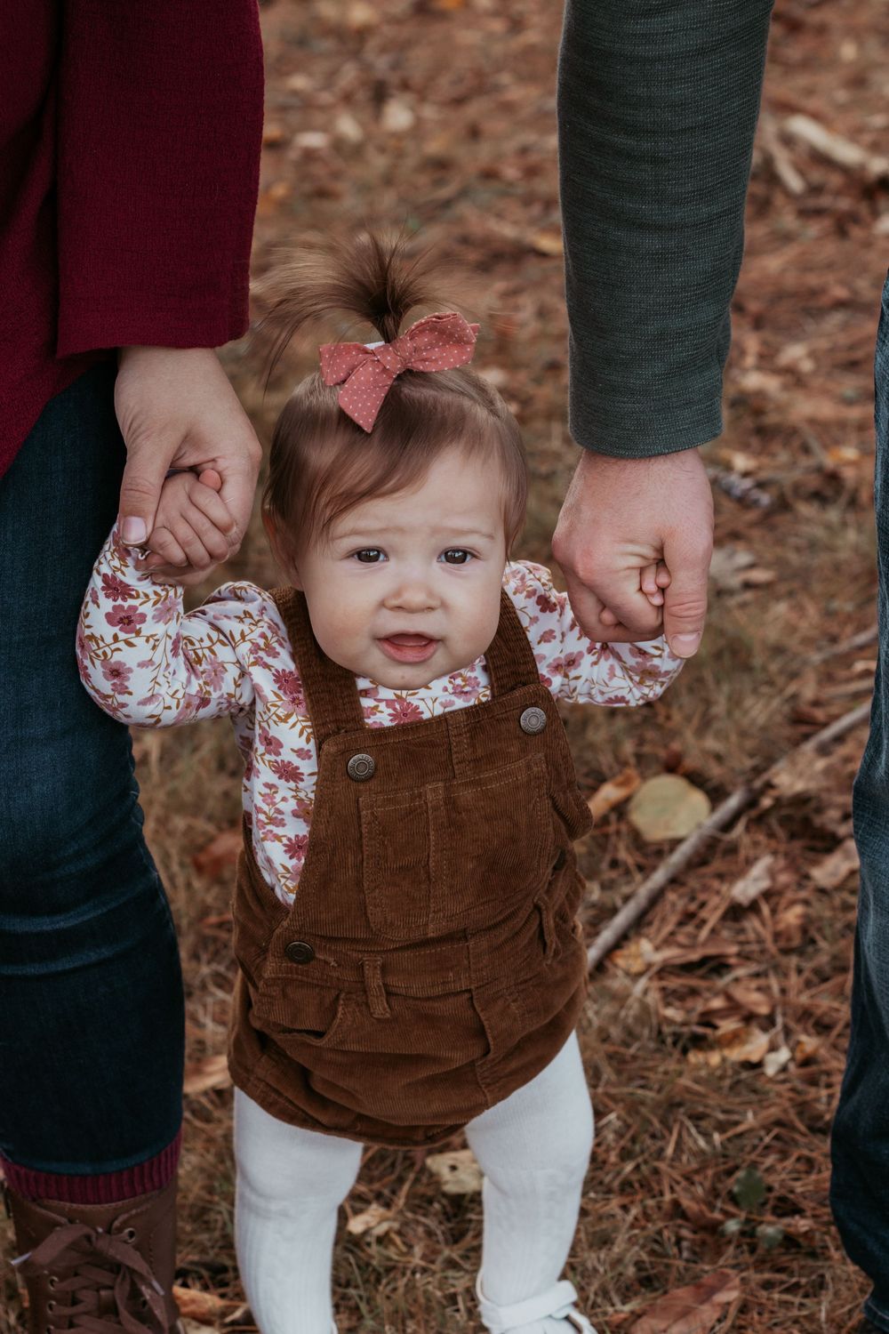 Close-up of baby wearing brown corduroy overalls held by parents outdoors.