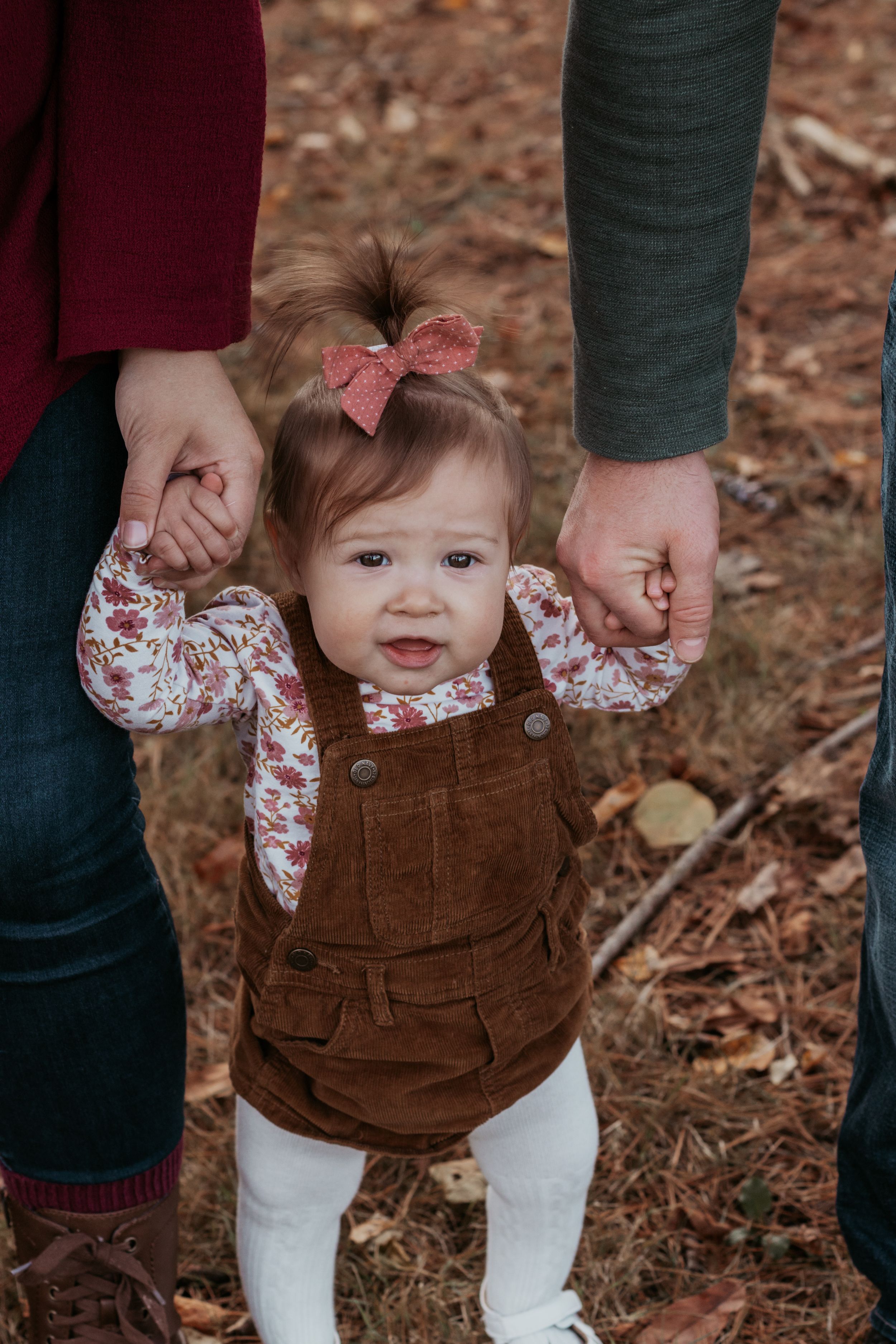 Close-up of baby wearing brown corduroy overalls held by parents outdoors.