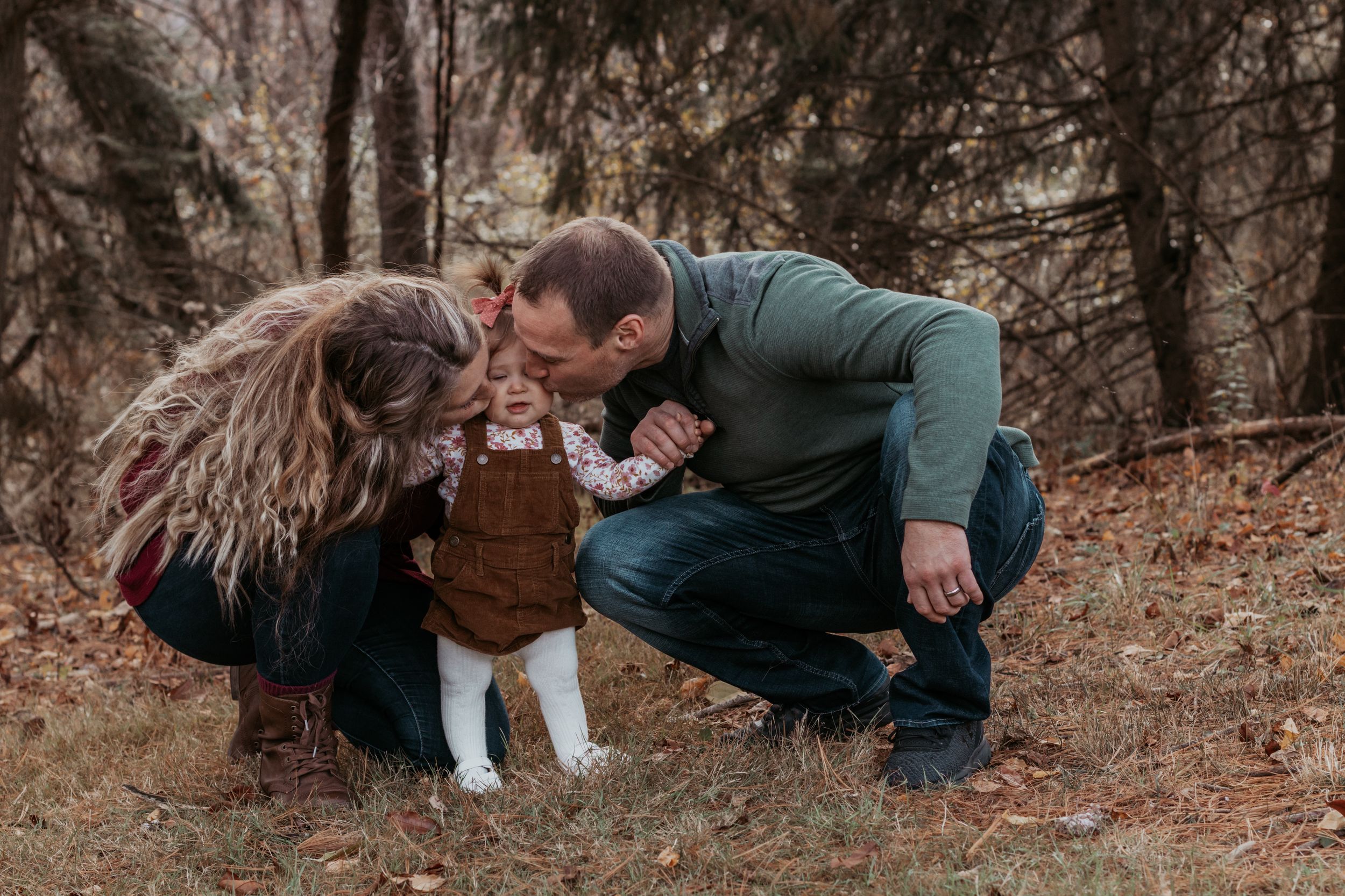 A playful family photo session in a wooded area during autumn with people lying on fallen leaves.