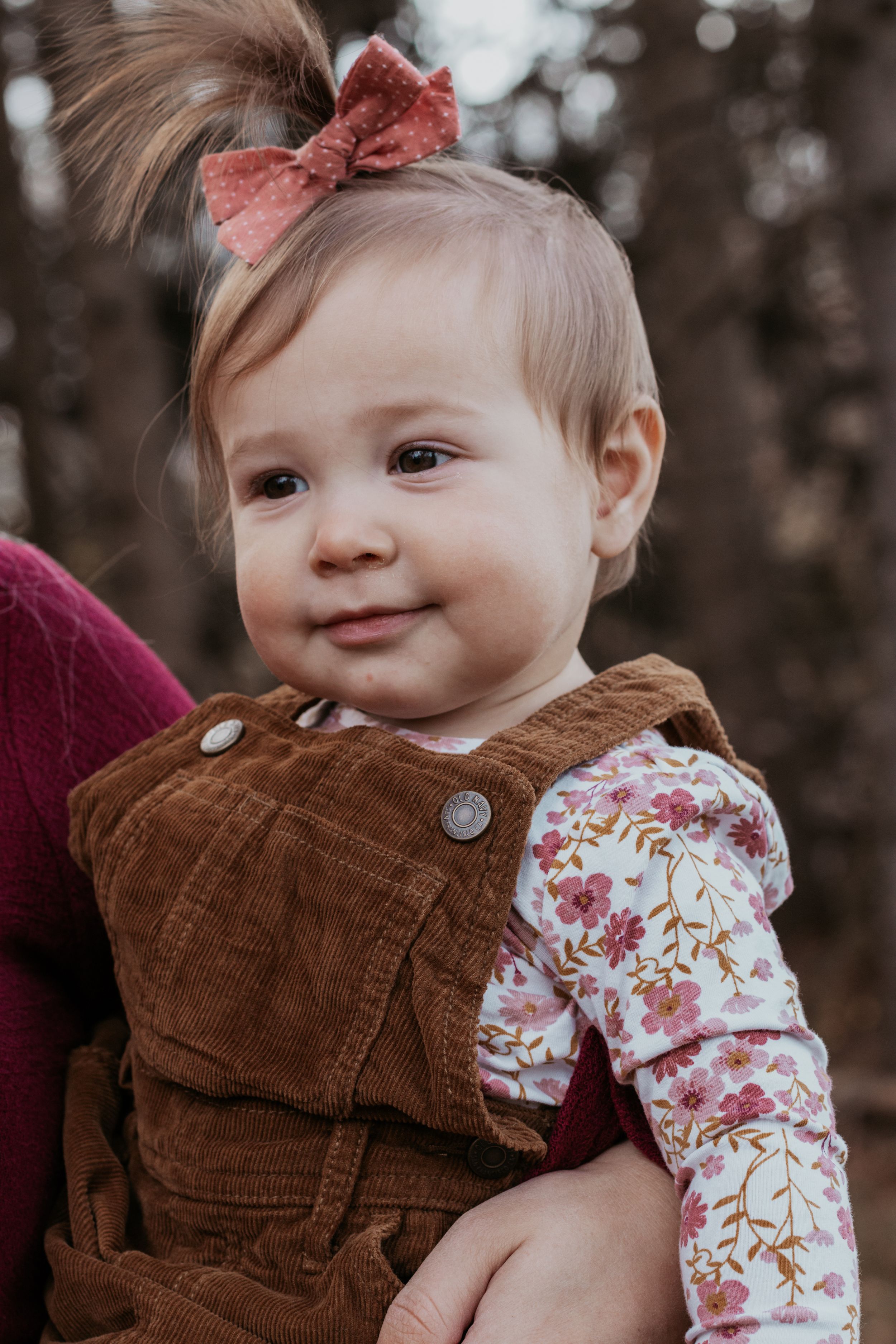 Baby wearing brown corduroy overalls and floral shirt smiles sweetly at camera.