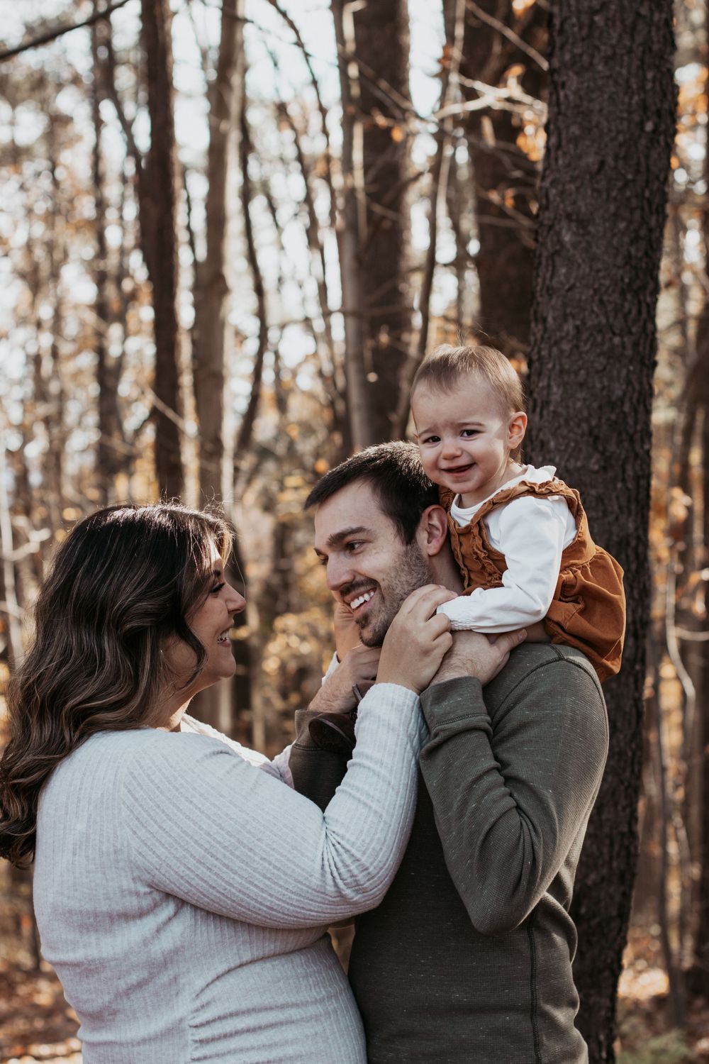Family sharing playful moments with their baby in a wooded autumn setting.