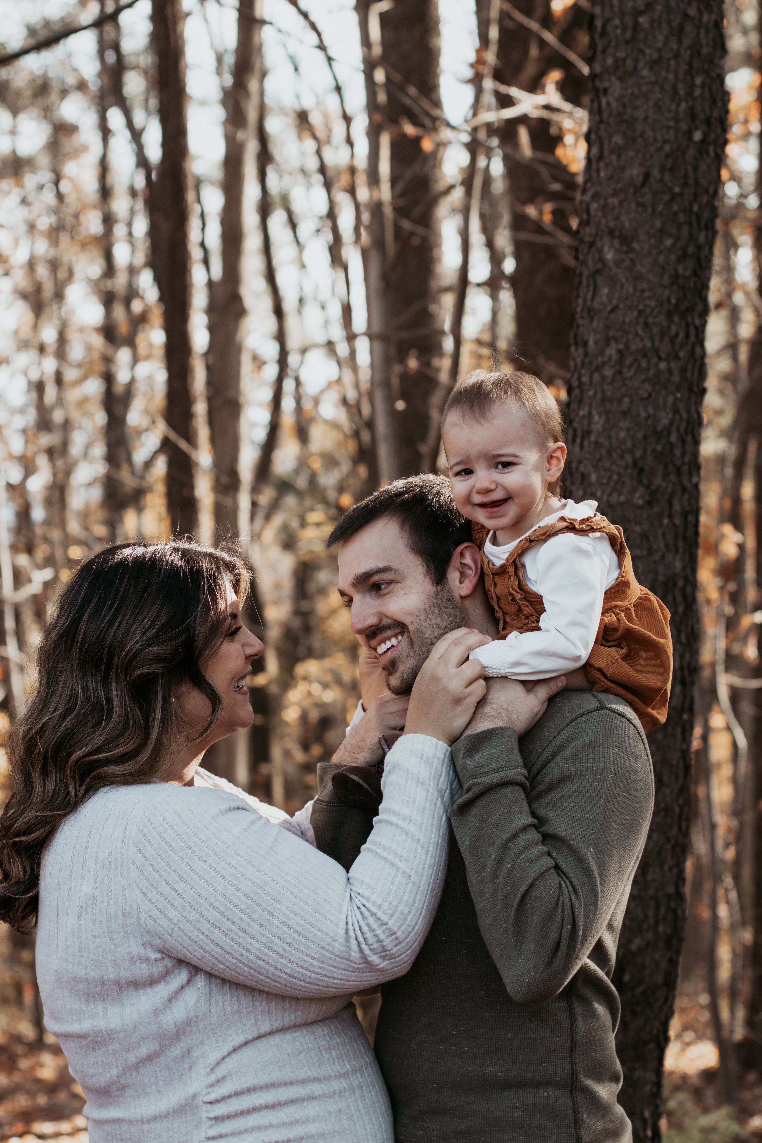 Family sharing playful moments with their baby in a wooded autumn setting.