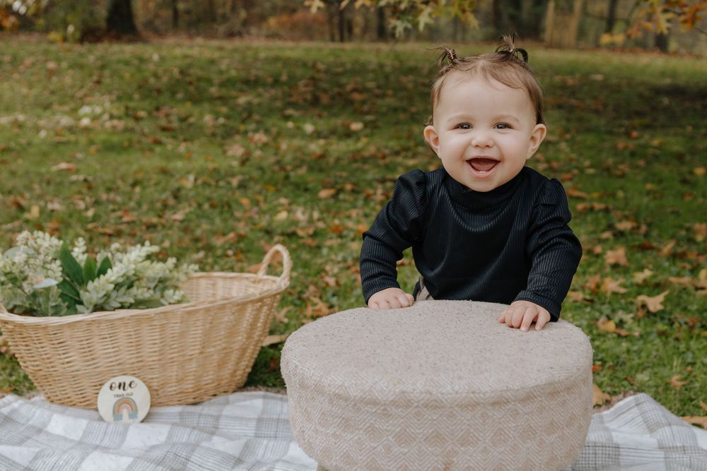 Child smiling next to wicker basket and ottoman during outdoor autumn photoshoot.