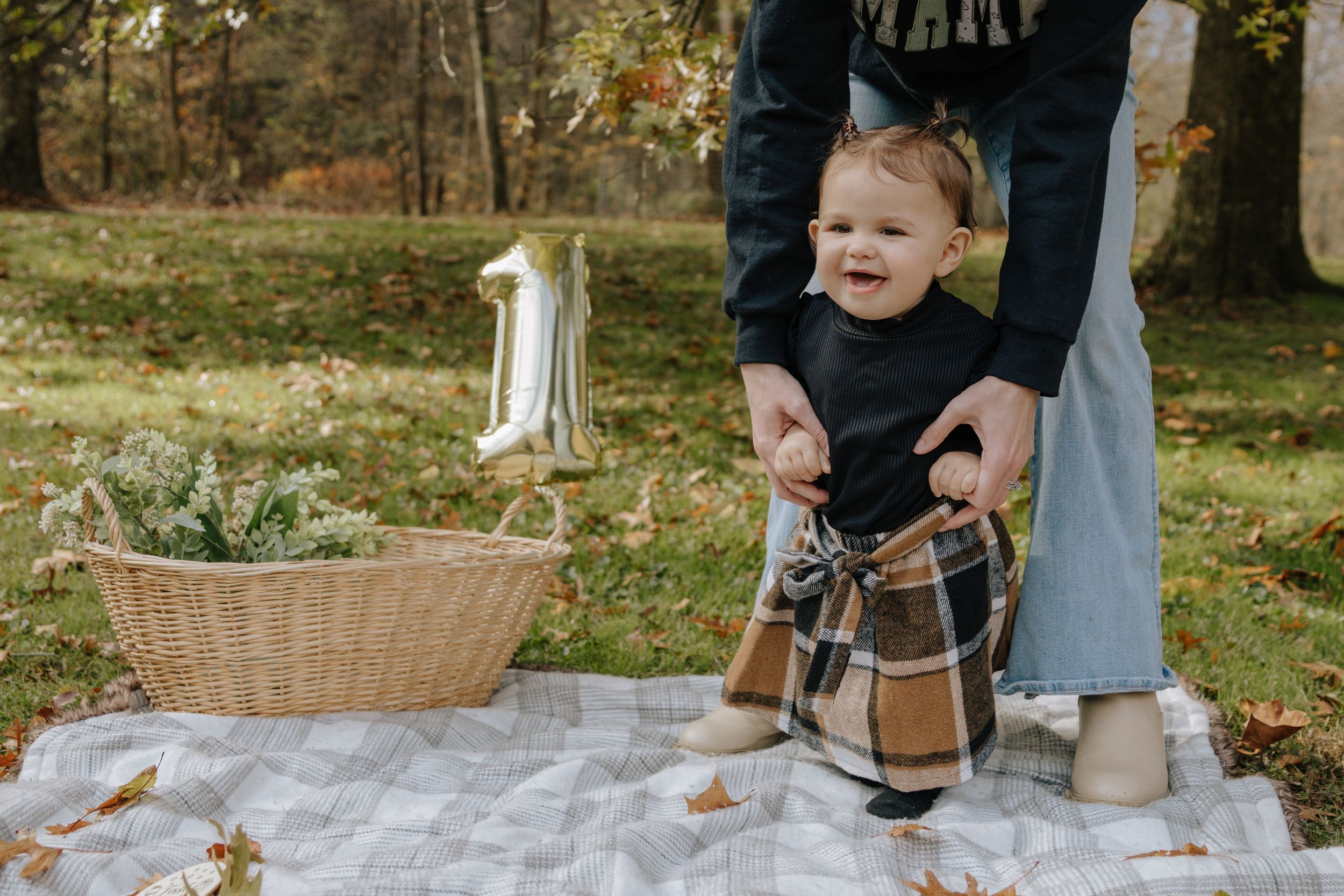Child laughing while being supported on picnic blanket during autumn photoshoot.