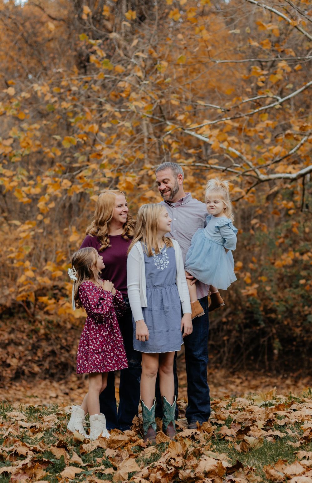 Family enjoying autumn photoshoot among fallen leaves in forest setting.