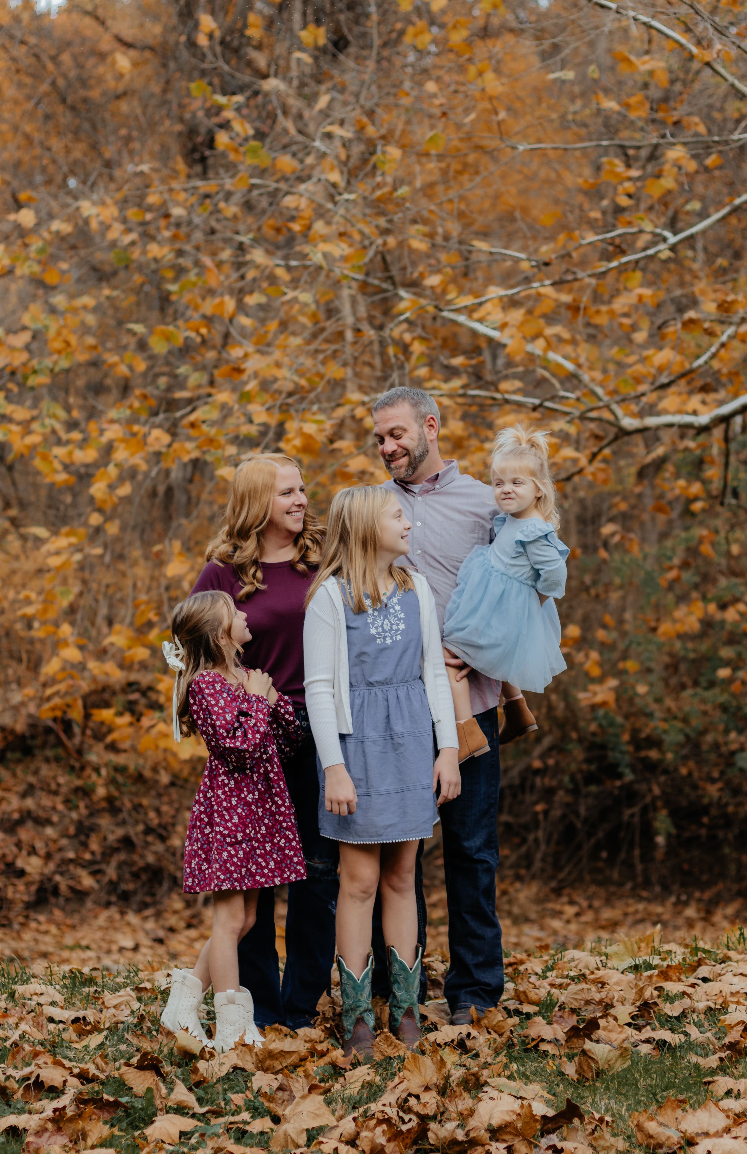 Family enjoying autumn photoshoot among fallen leaves in forest setting.