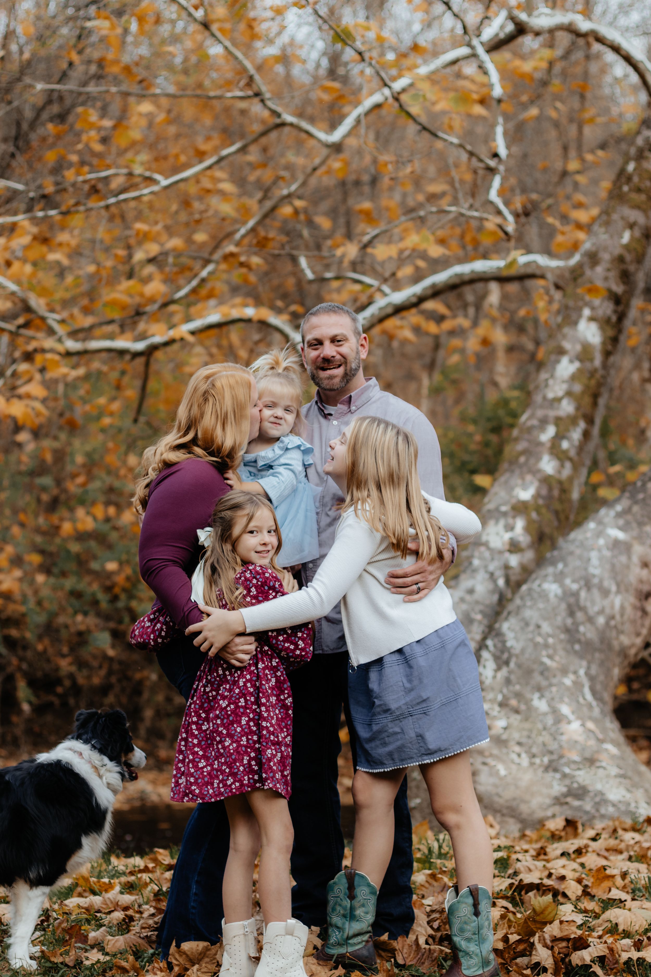 A joyful autumn family photoshoot with a dog in a forest setting filled with fallen leaves and warm colors.