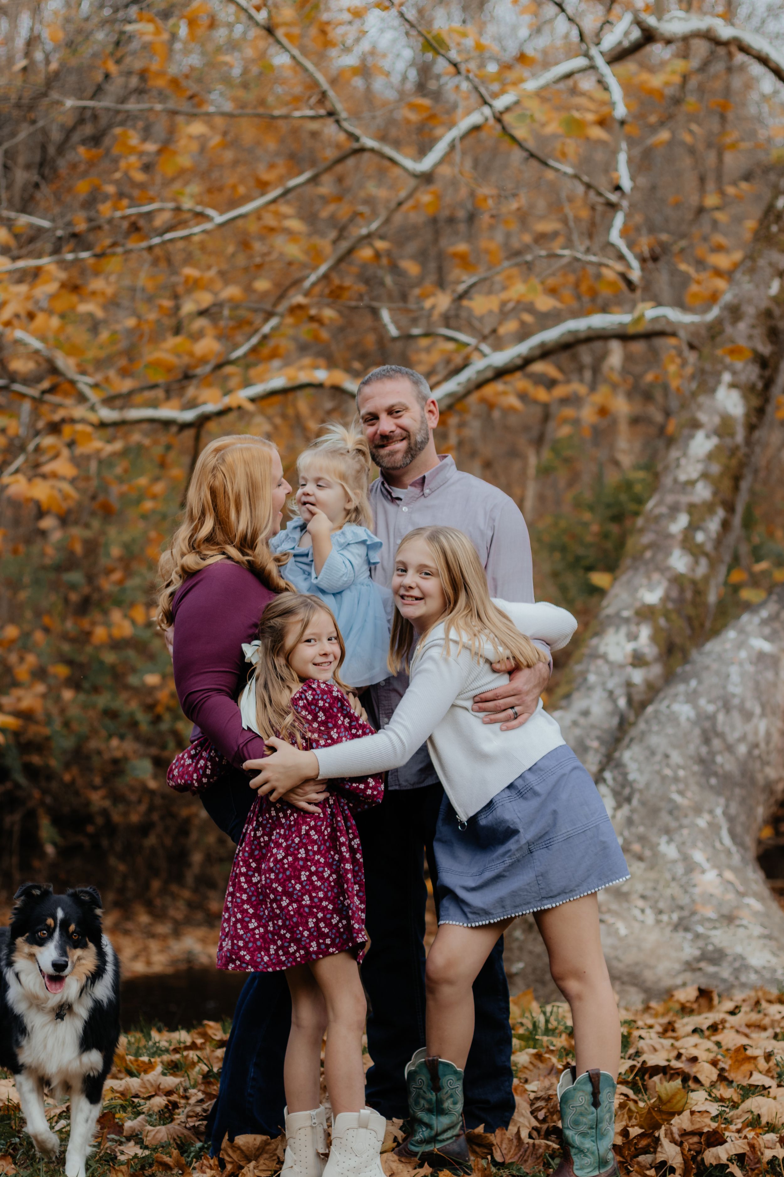 Candid family moment captured in the woods during fall with playful poses and a border collie watching.