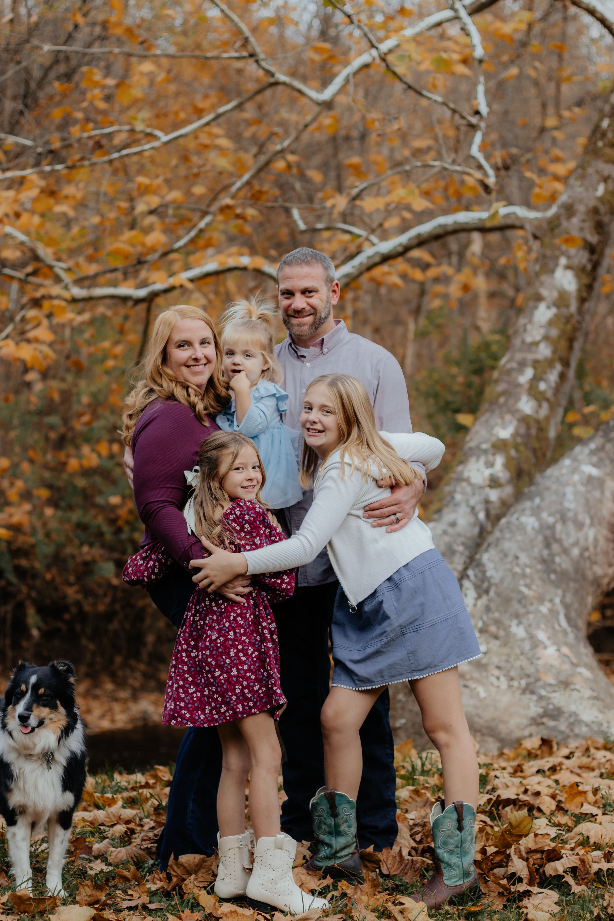 Family enjoying a fun photo session in autumn woods with their border collie among fallen leaves.