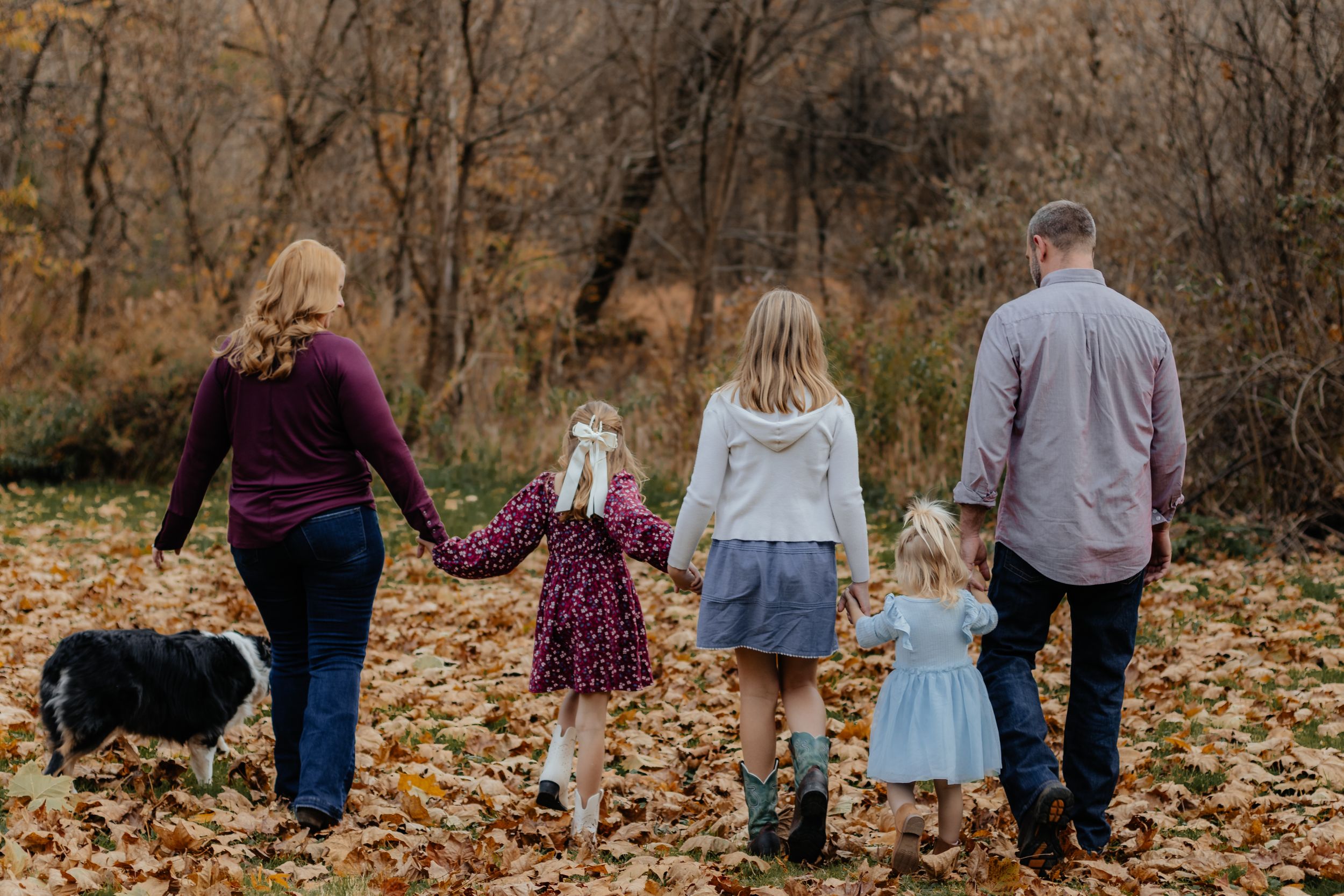 A family walks together through autumn leaves on a forest path during fall.