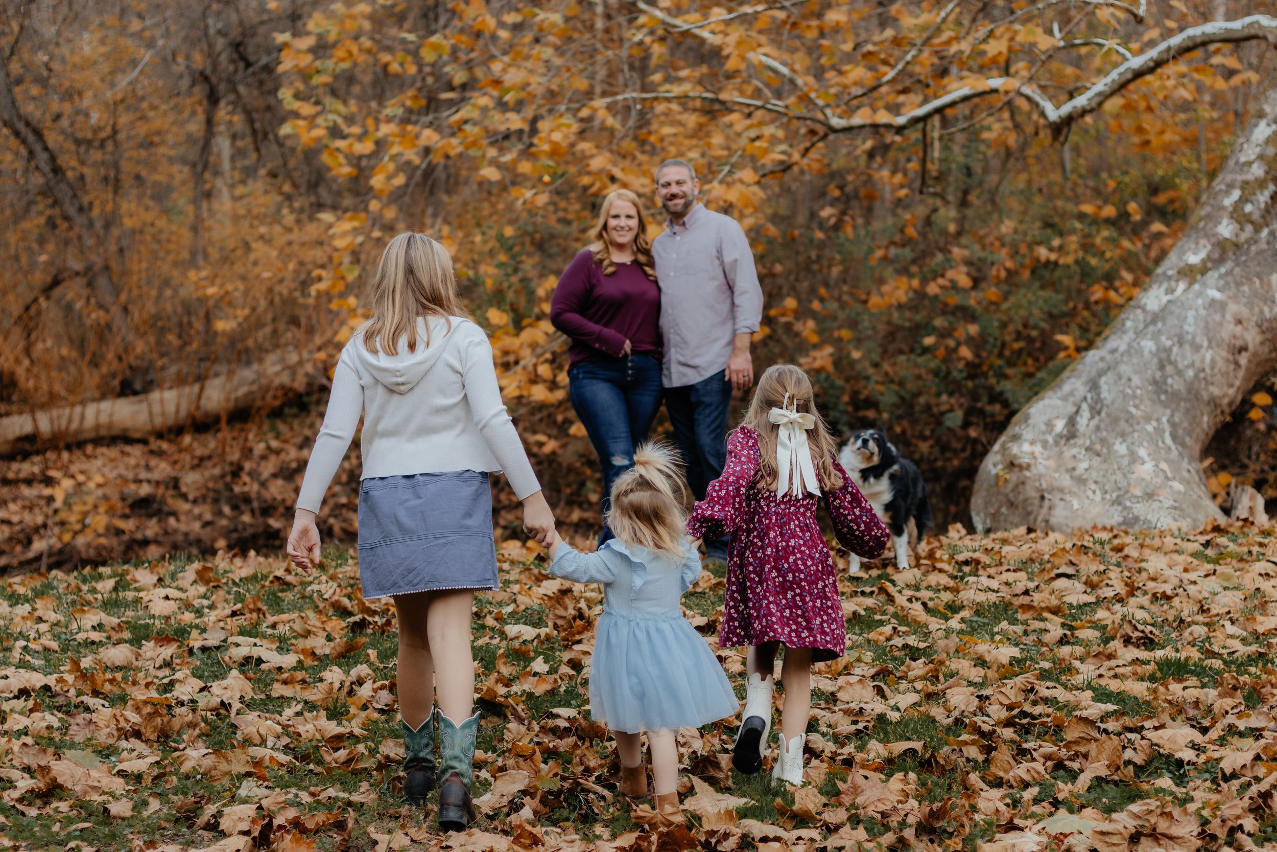 Family members walking together through wooded area with autumn colors visible.