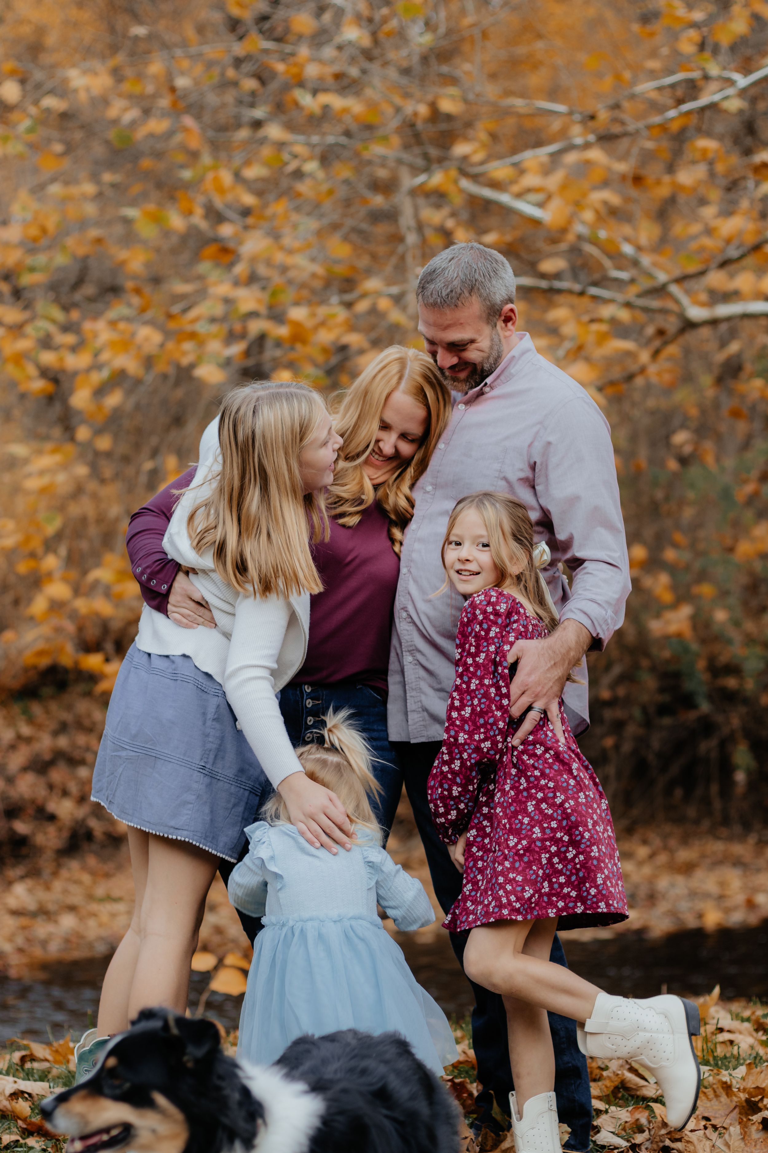 Family shares joyful moments together with their black and white dog among fallen autumn leaves.