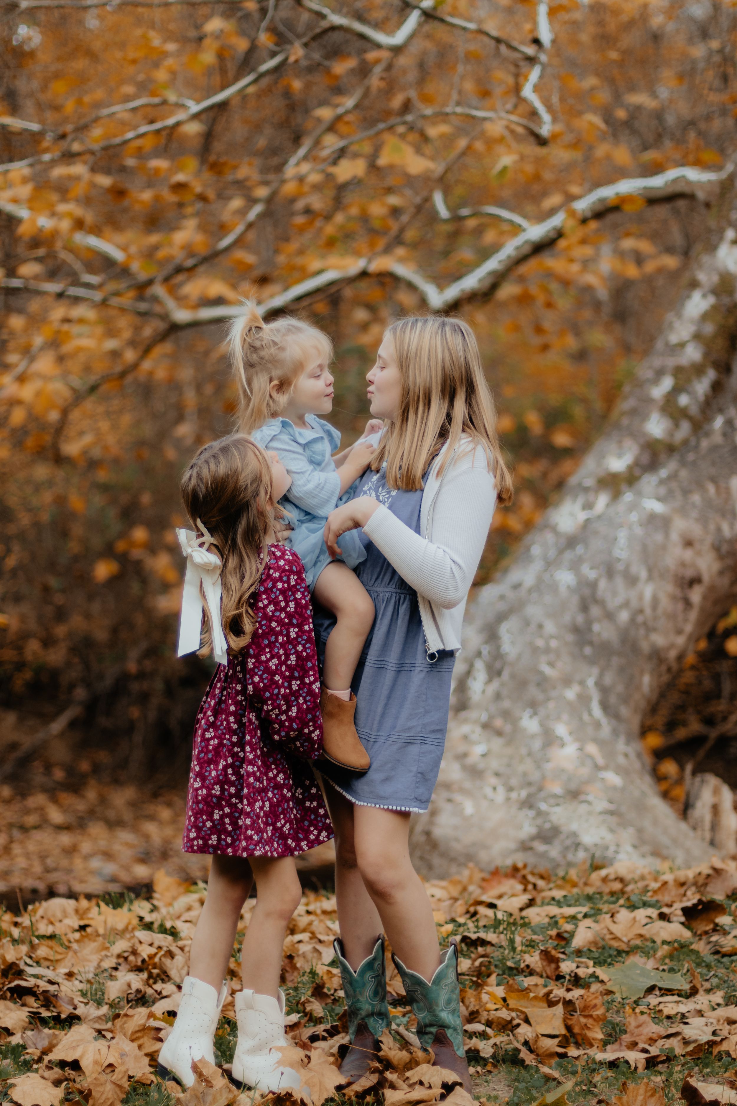 Children play together in fallen leaves wearing autumn outfits and boots.