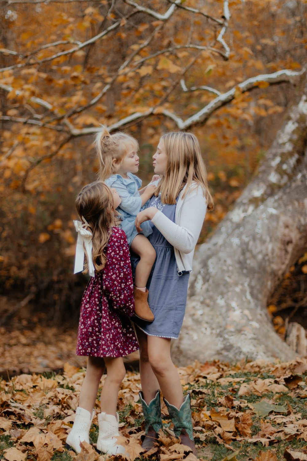 Children play together in fallen leaves wearing autumn outfits and boots.