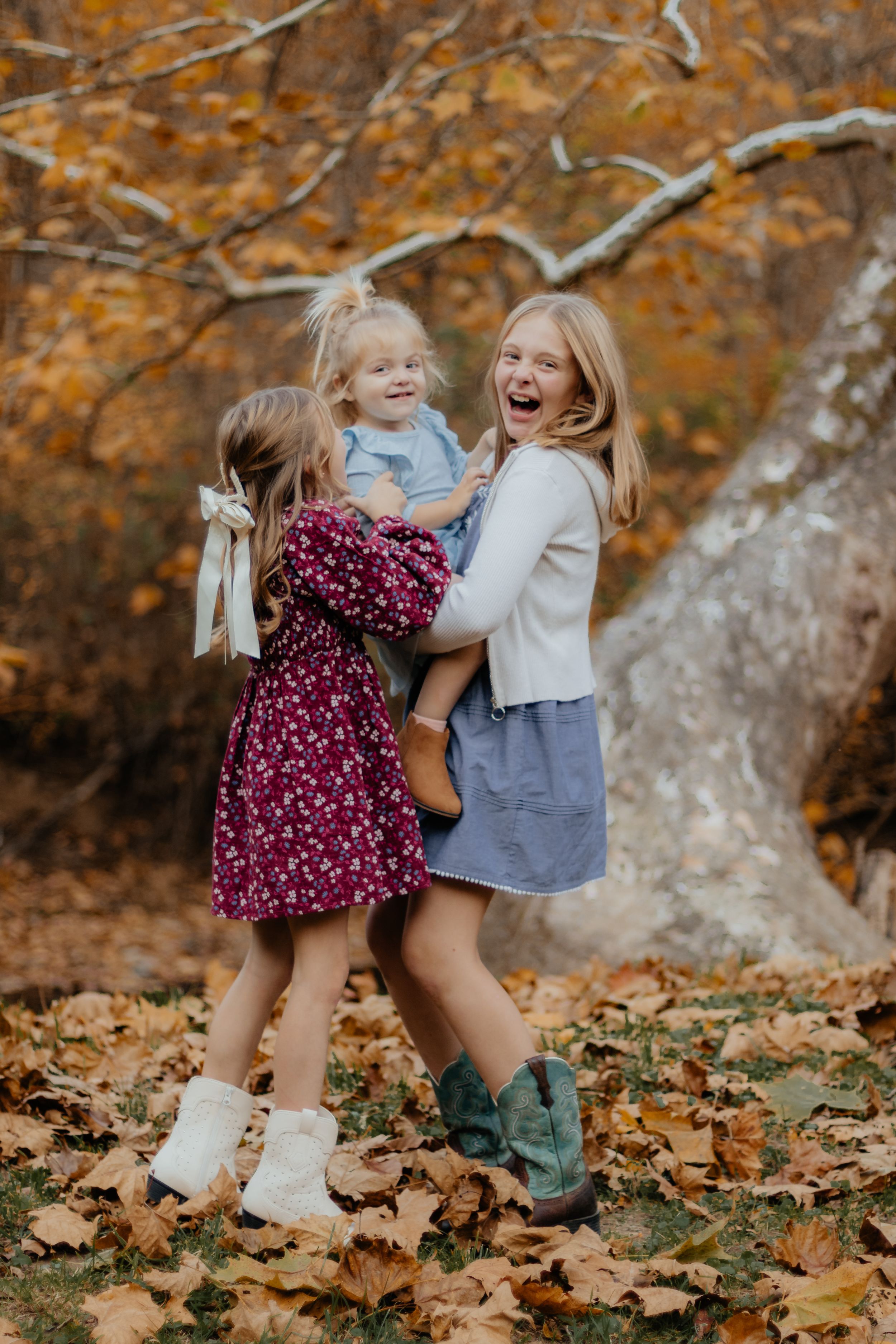 Three people sharing joyful laughter together among fallen autumn leaves in a forest setting.