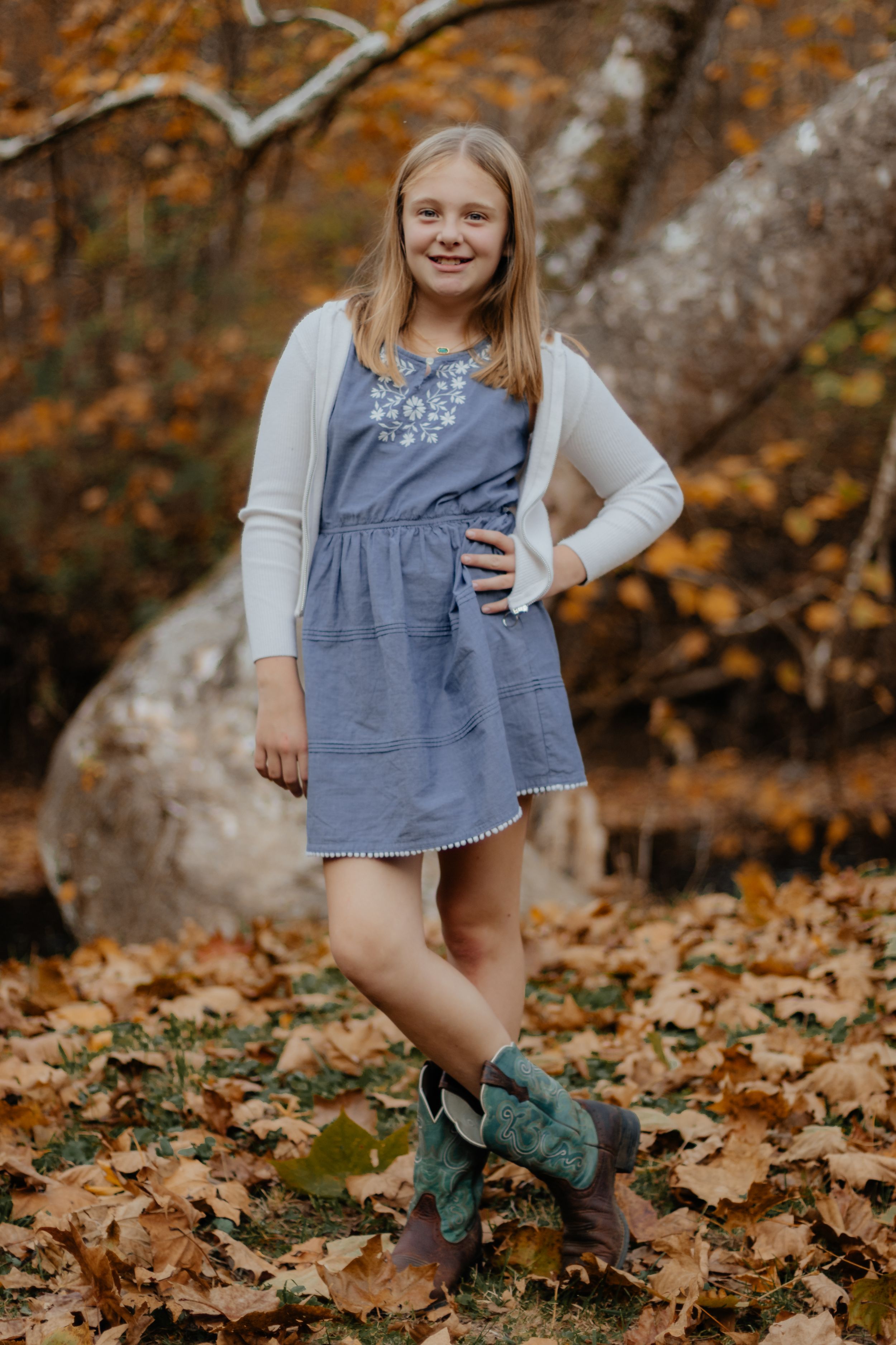 Casual pose in denim dress and green boots among autumn leaves.