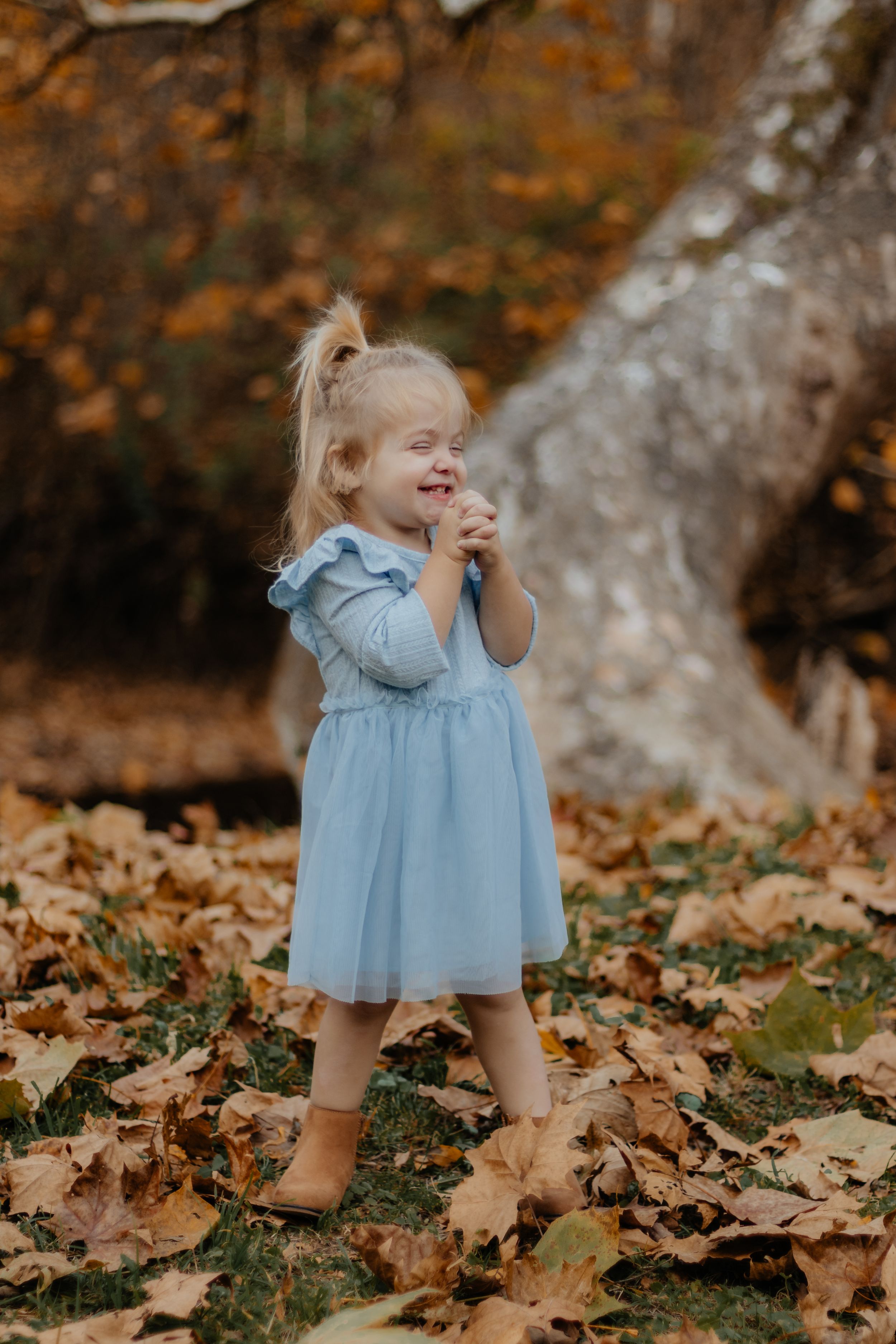Playful moment in light blue dress standing on fallen autumn leaves.