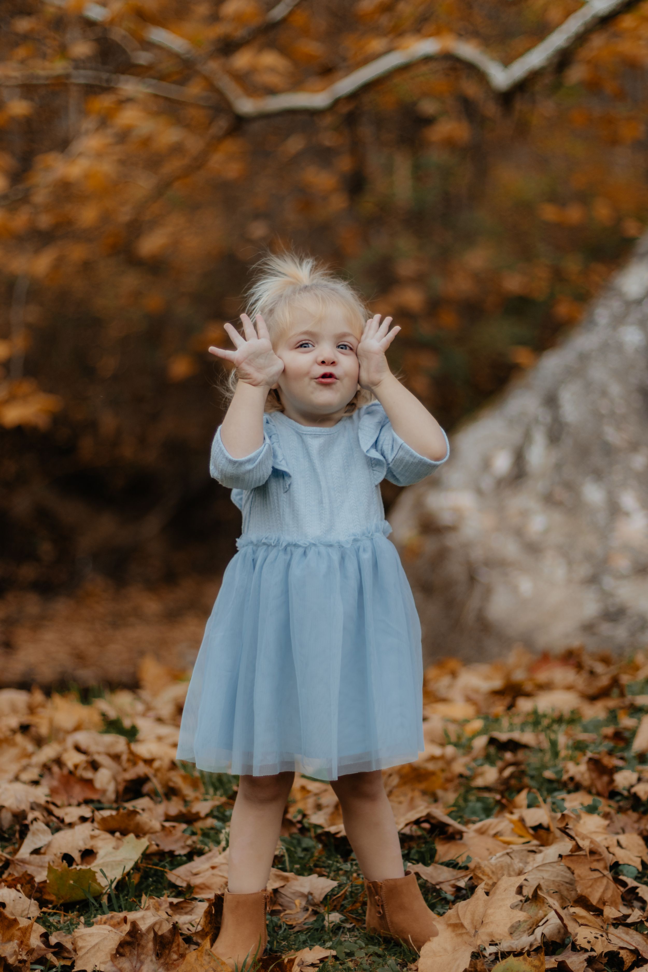 Playful stance in blue dress with hands up against fall foliage.