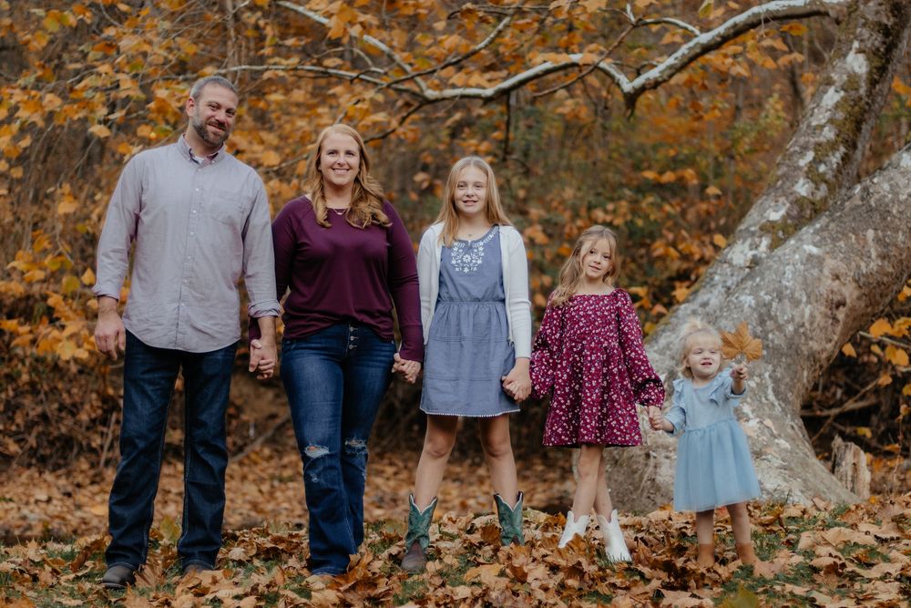 Family of five standing together against vibrant autumn forest backdrop.