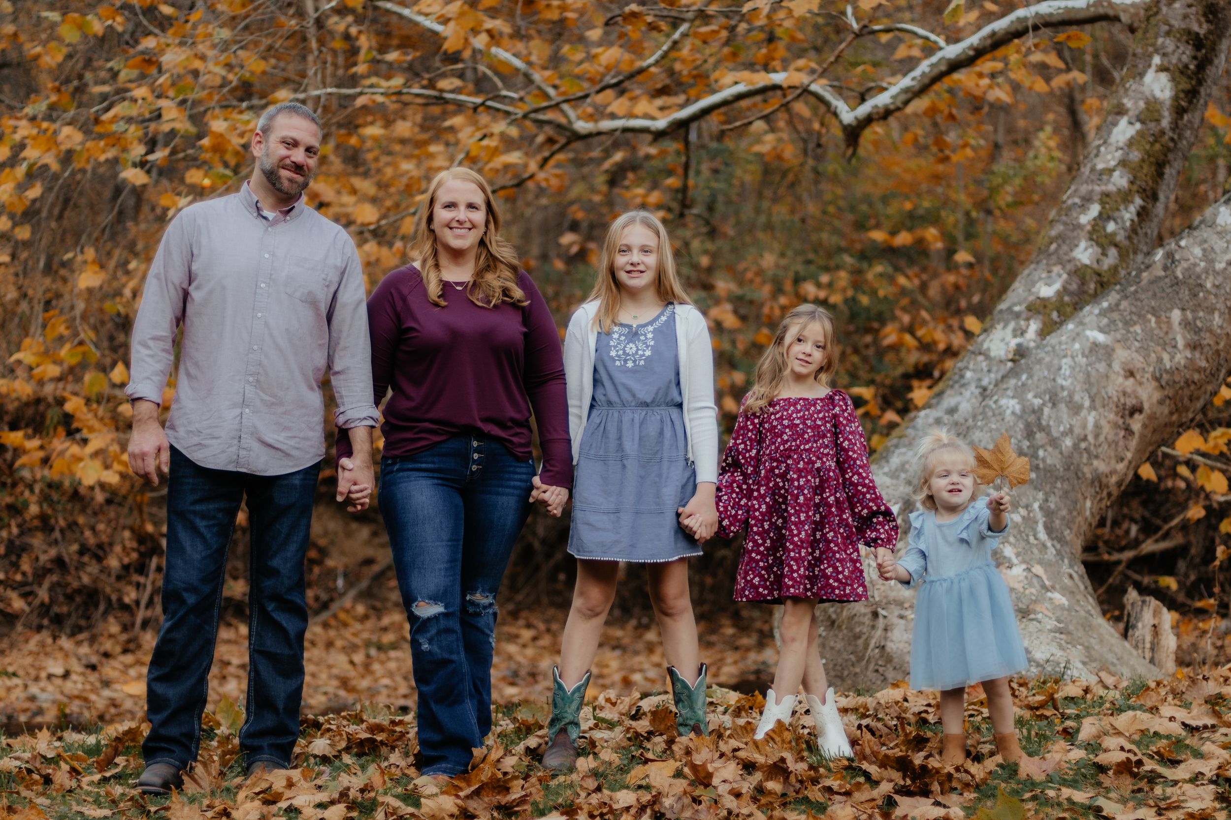 Family of five standing together against vibrant autumn forest backdrop.