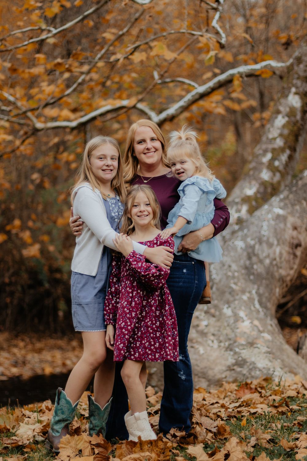 A group poses together against a backdrop of fall colors and a large tree trunk.