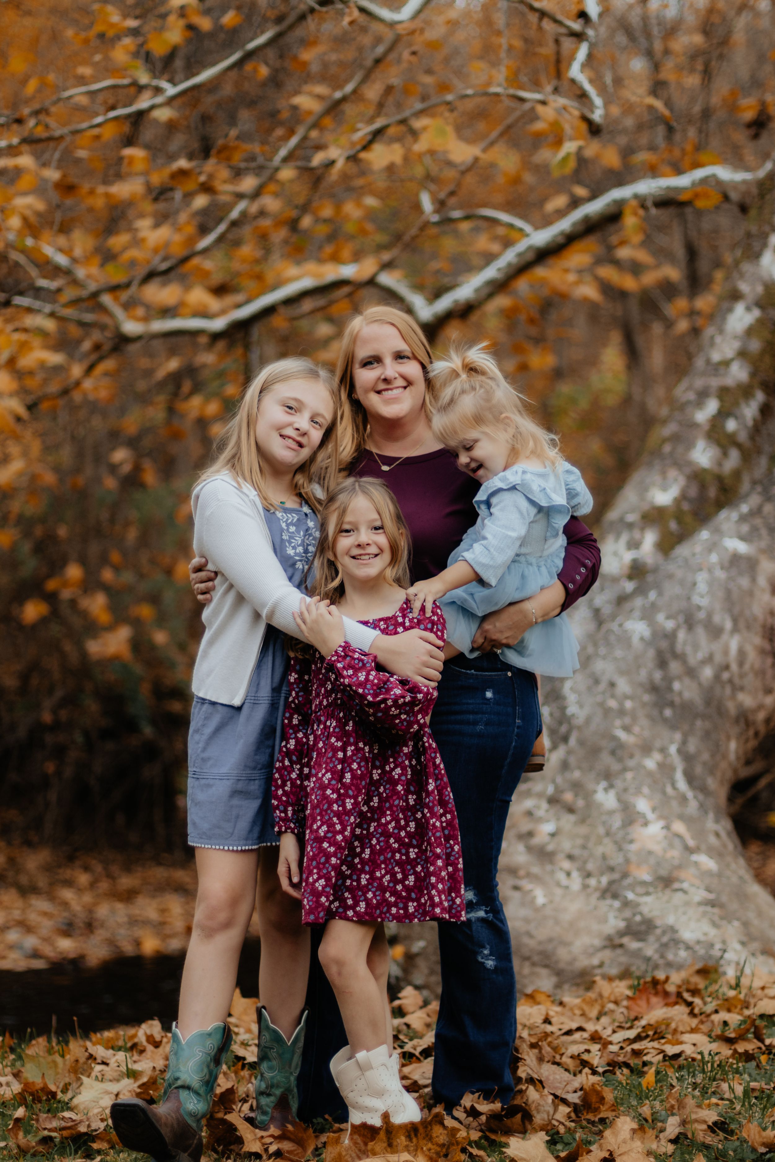 A group shares a warm embrace while standing on fallen leaves in an autumn setting.