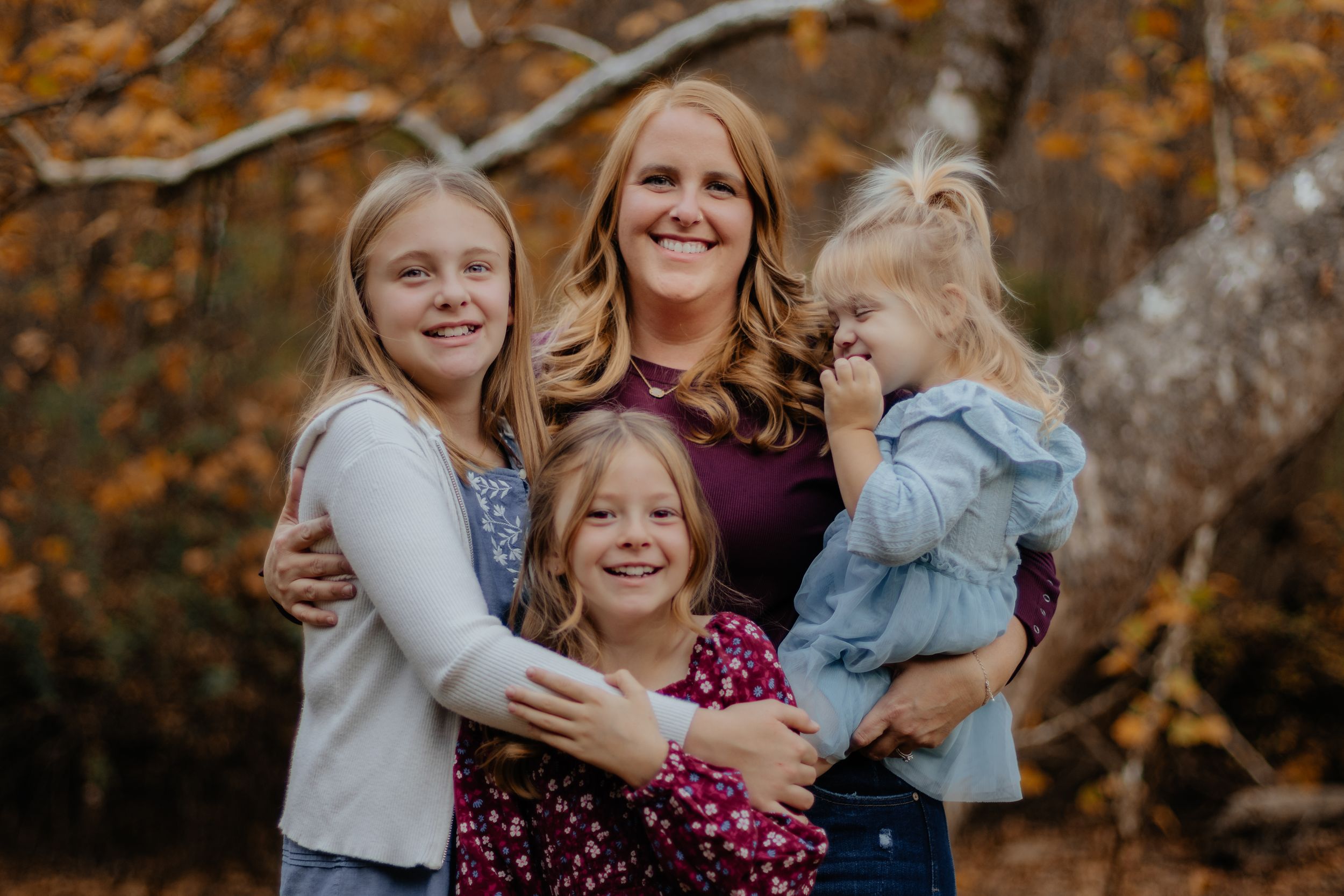 A group shares joyful laughter while posing together against autumn foliage.
